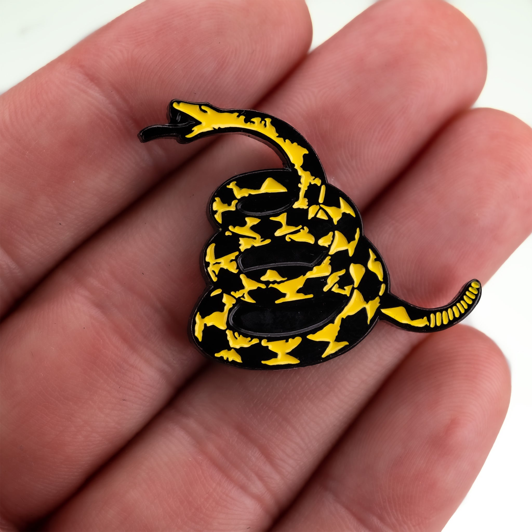 A hand holding a yellow and black "Don't Tread on Me" ball marker featuring a coiled snake design.