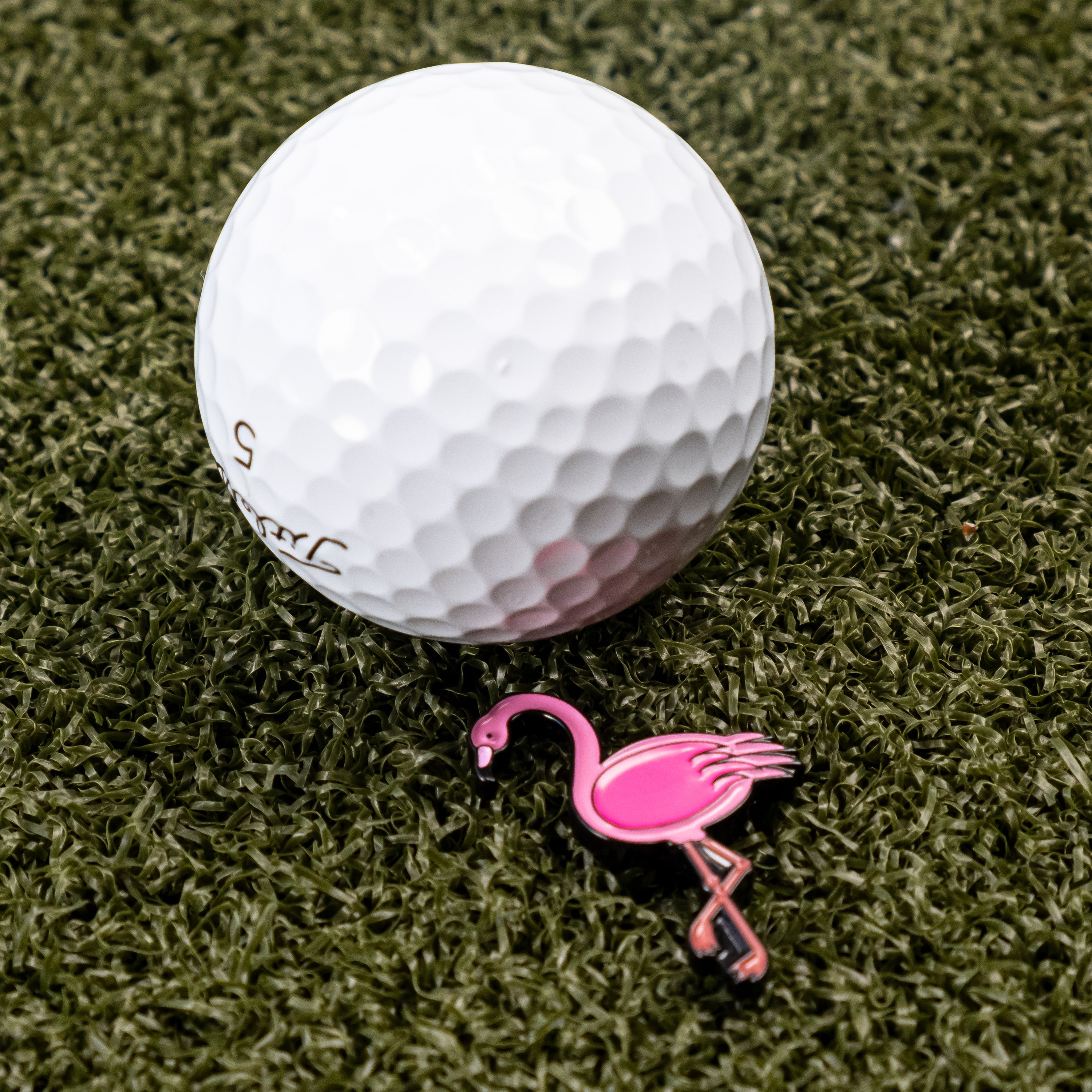 Flamingo ball marker next to a white golf ball on green turf, adding a fun touch to your golf game.