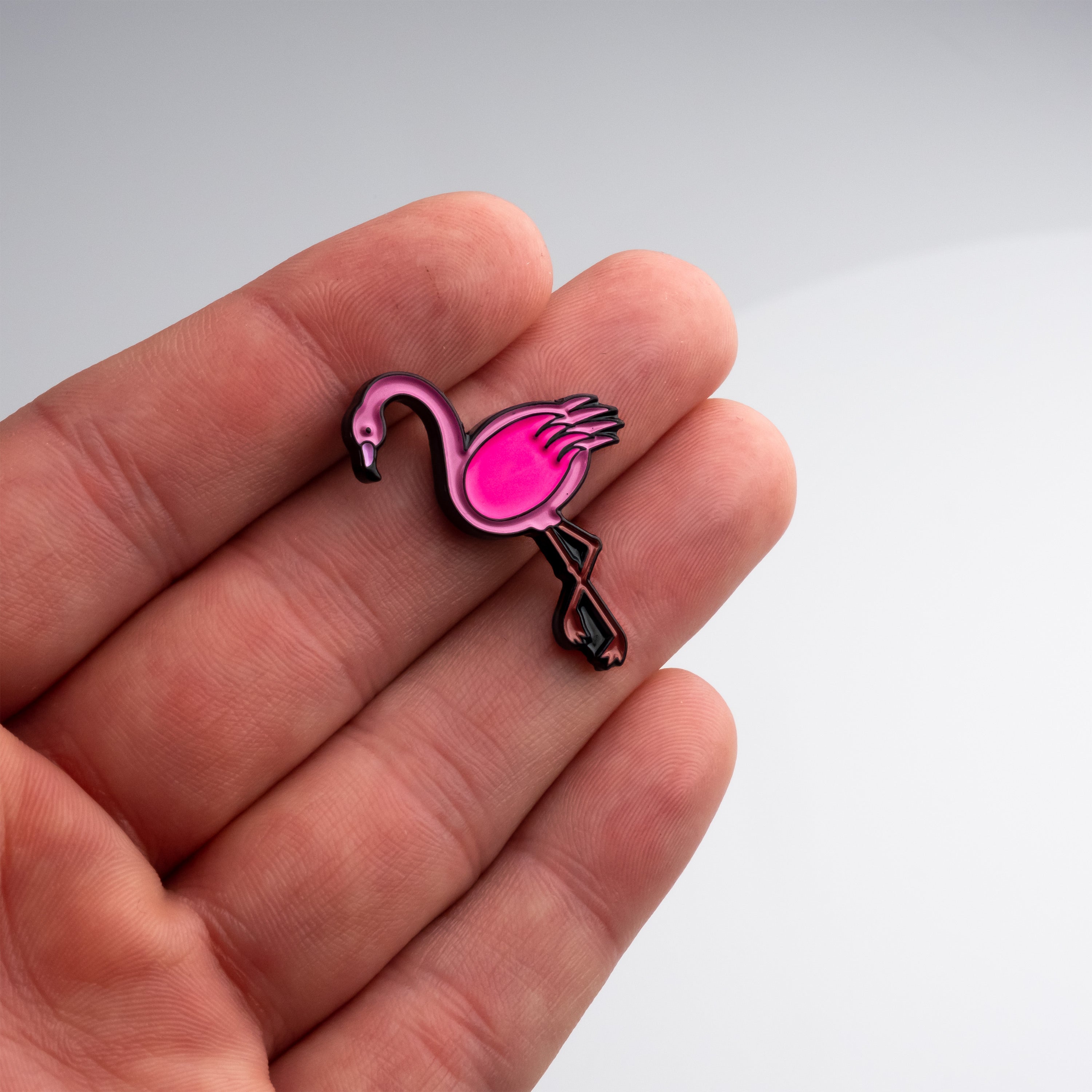 A hand holding a vibrant pink flamingo ball marker, showcasing its unique design for golfers.