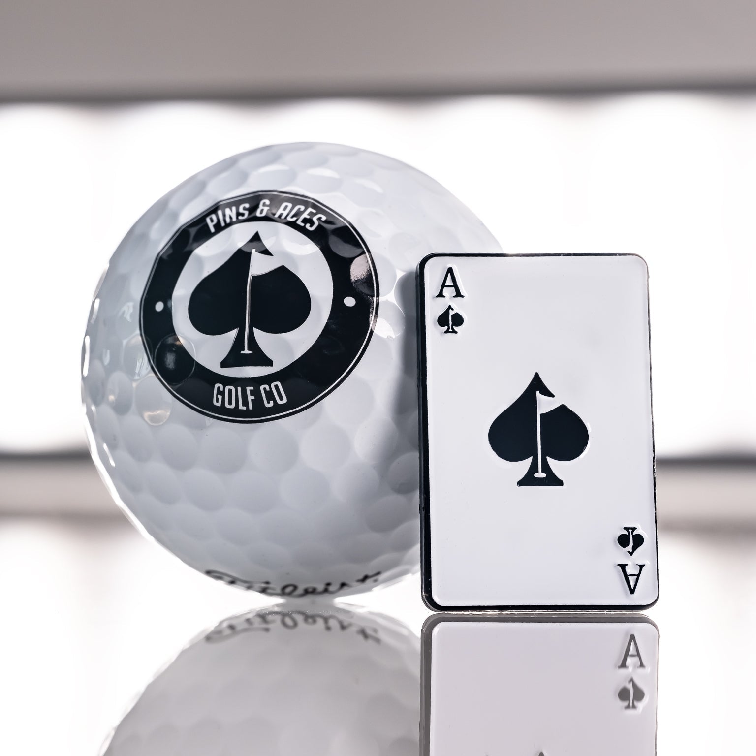 Ace of Spades ball marker next to a golf ball, featuring a bold spade logo and sleek design for stylish golfers.