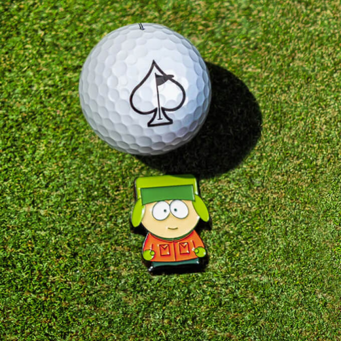 Golf ball with a black spade logo and a cartoon character golf tee marker on green grass, highlighting bold, playful golf ...