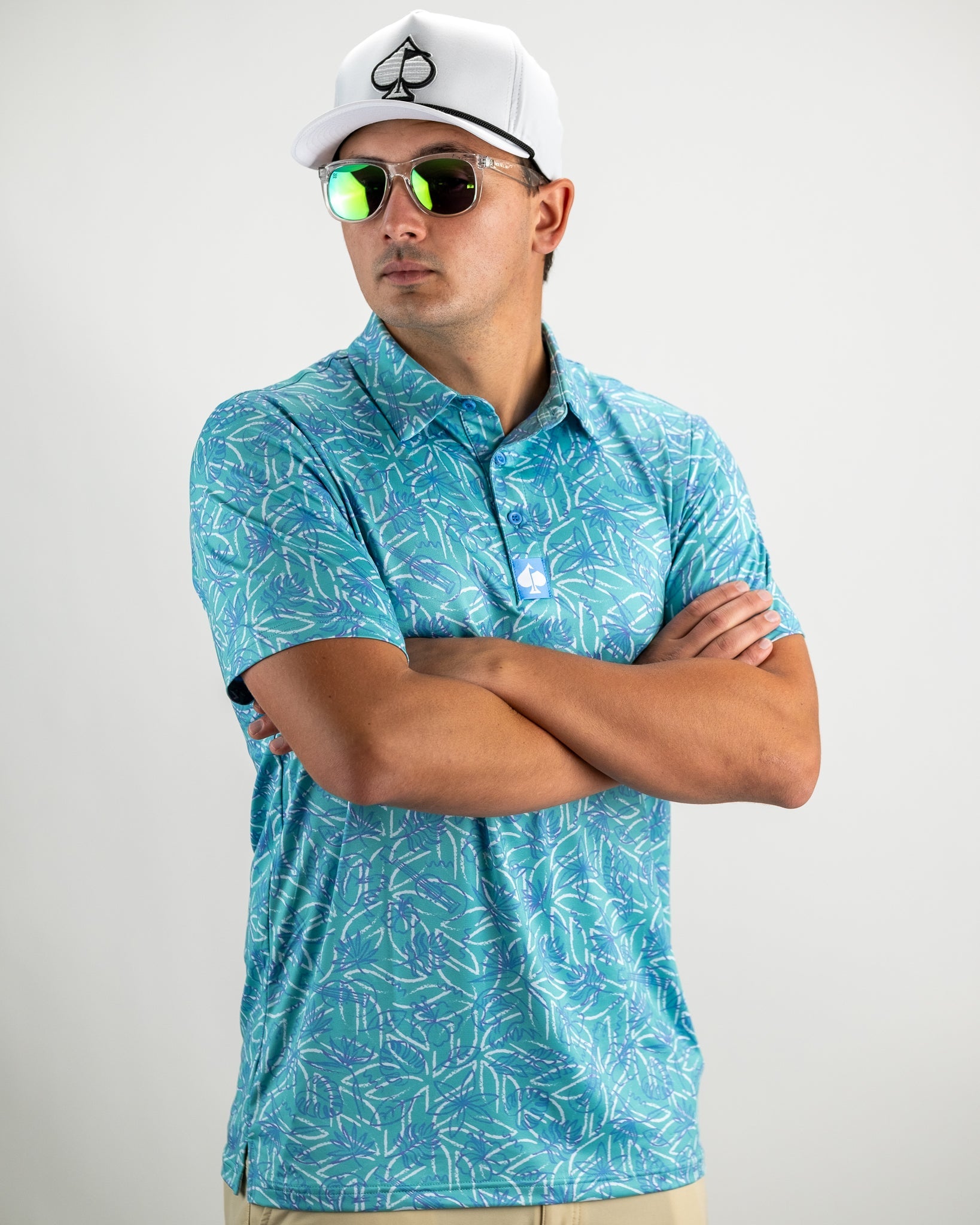 Men's Margaritaville 5 O'Clock Ocean polo shirt featuring a vibrant tropical pattern, worn with sunglasses and a white cap.