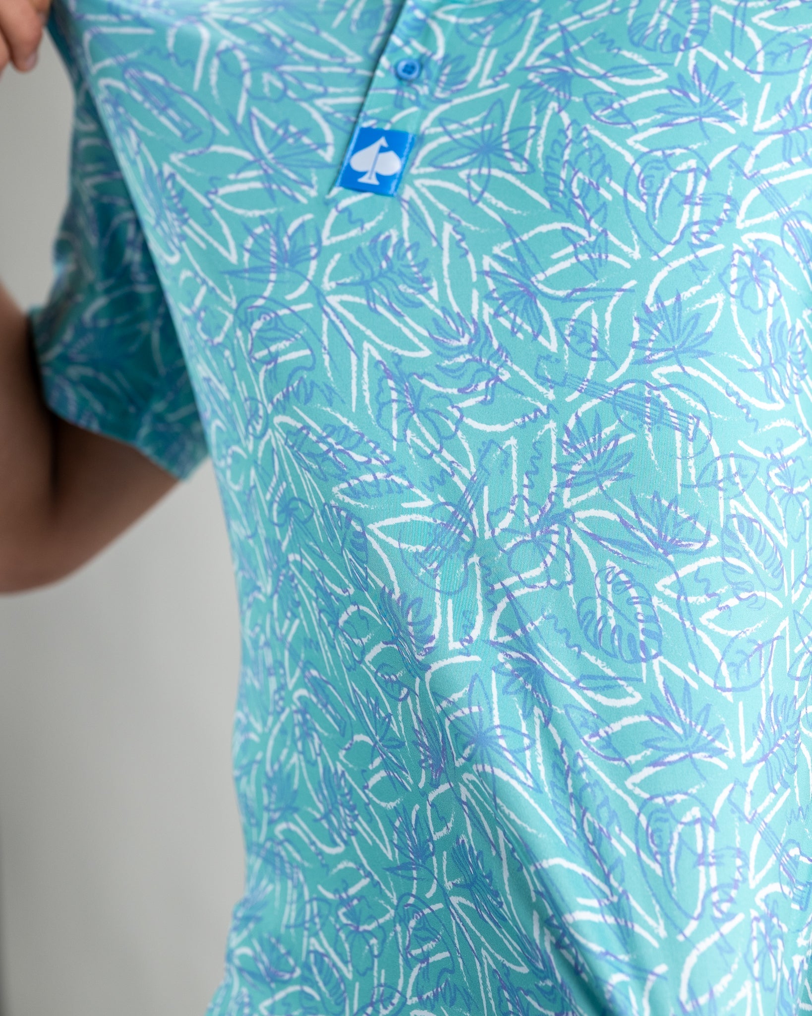 Light blue polo shirt featuring a vibrant tropical pattern with palm leaves and ocean elements, perfect for casual golf outings.