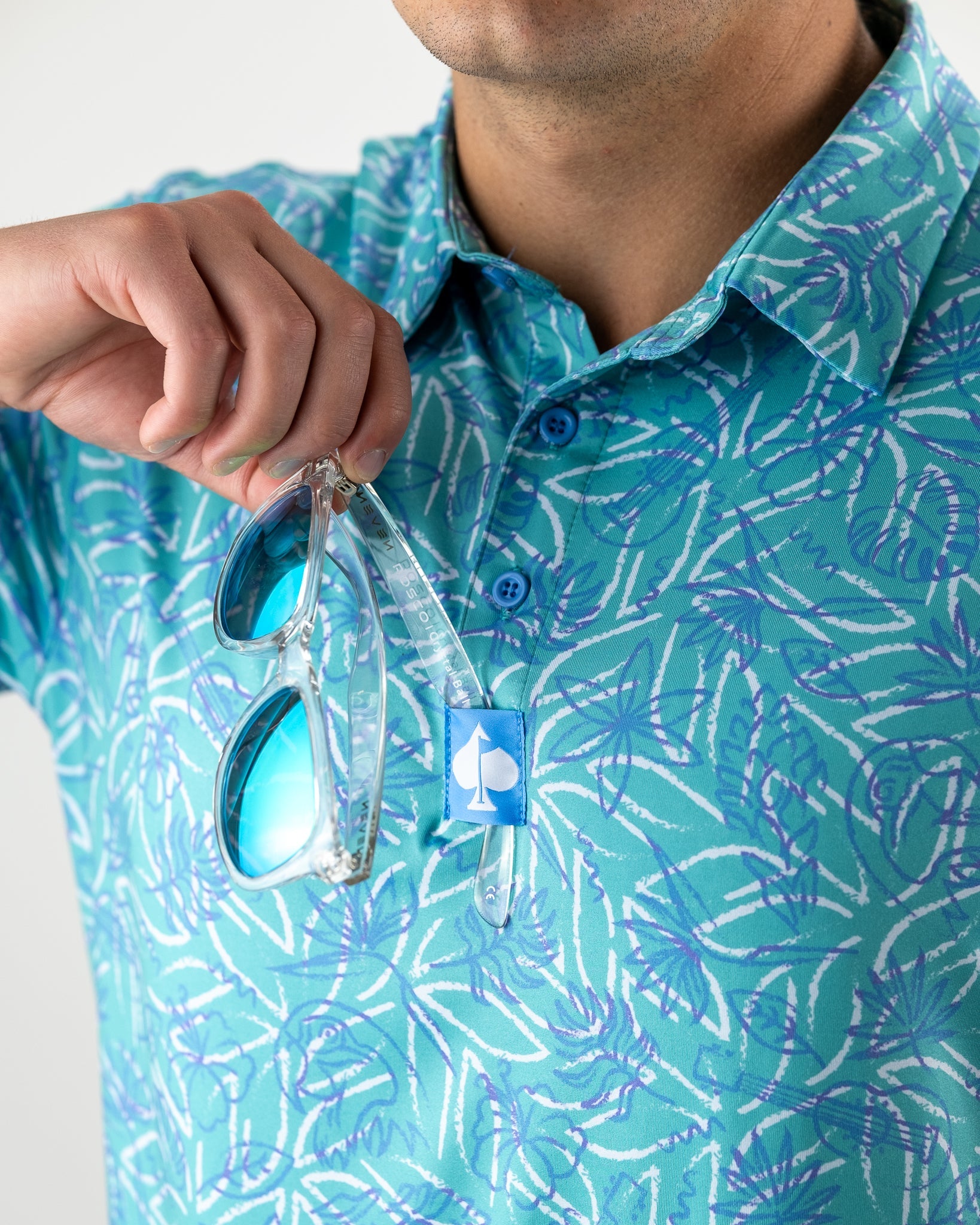 Man holding sunglasses while wearing a vibrant blue and green patterned polo shirt from Margaritaville.