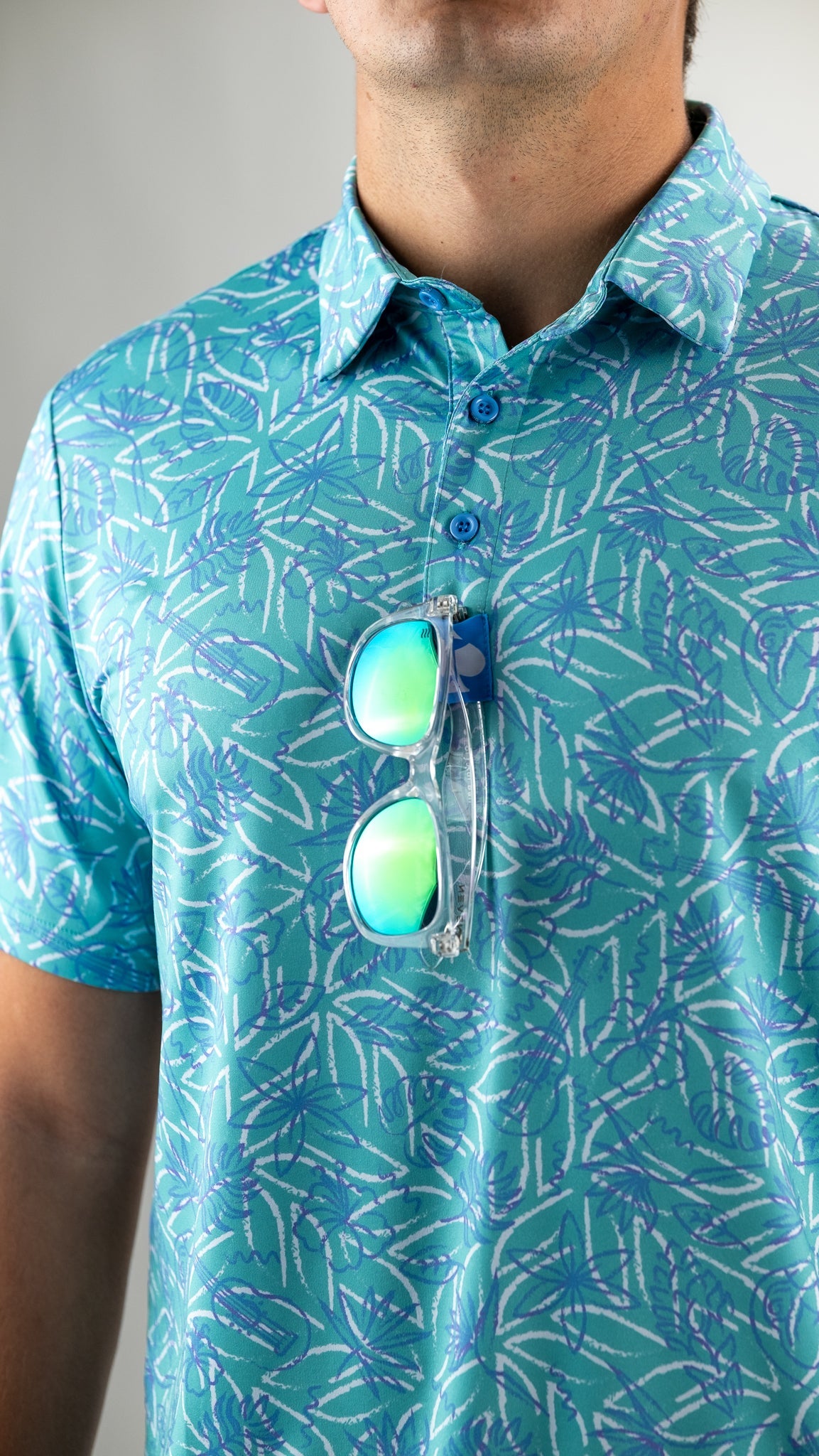 Men's Margaritaville 5 O'Clock Ocean polo shirt featuring a vibrant tropical pattern, paired with stylish sunglasses.