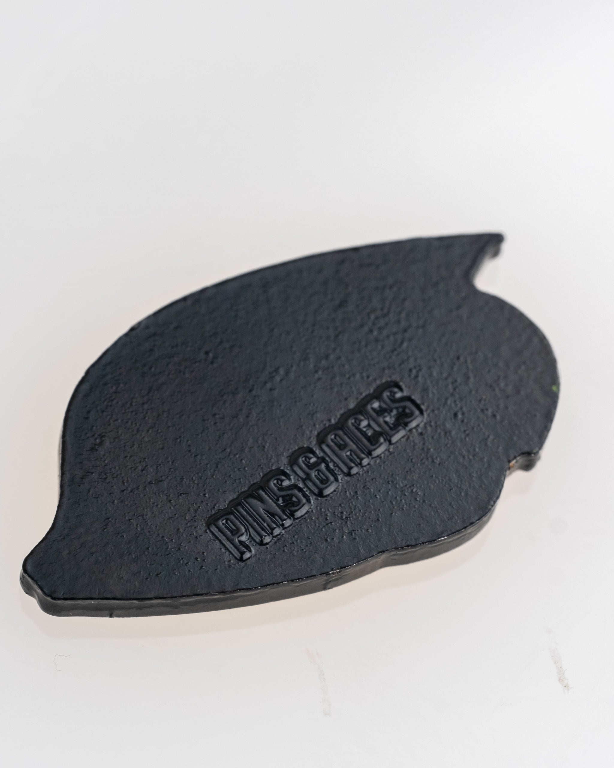 Black angel fish-shaped ball marker with "PINS & ACES" embossed on the surface, ideal for stylish golf accessories.