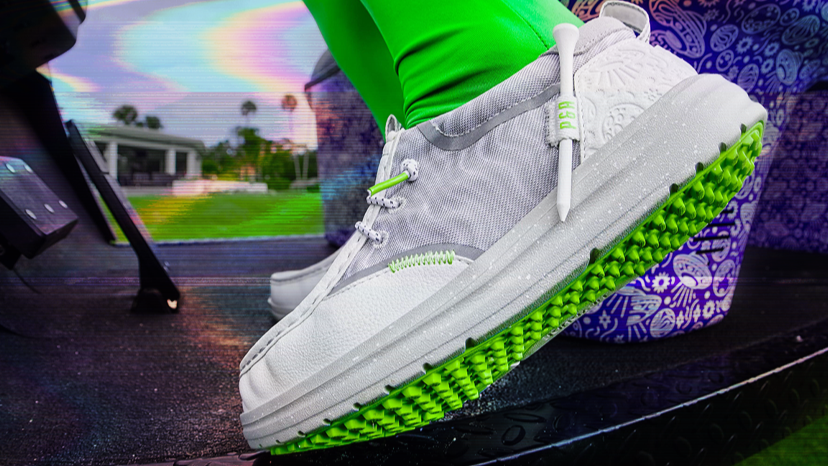 Close-up of a white and gray golf shoe with neon green sole and accents, worn with bright green golf pants on a colorful c...