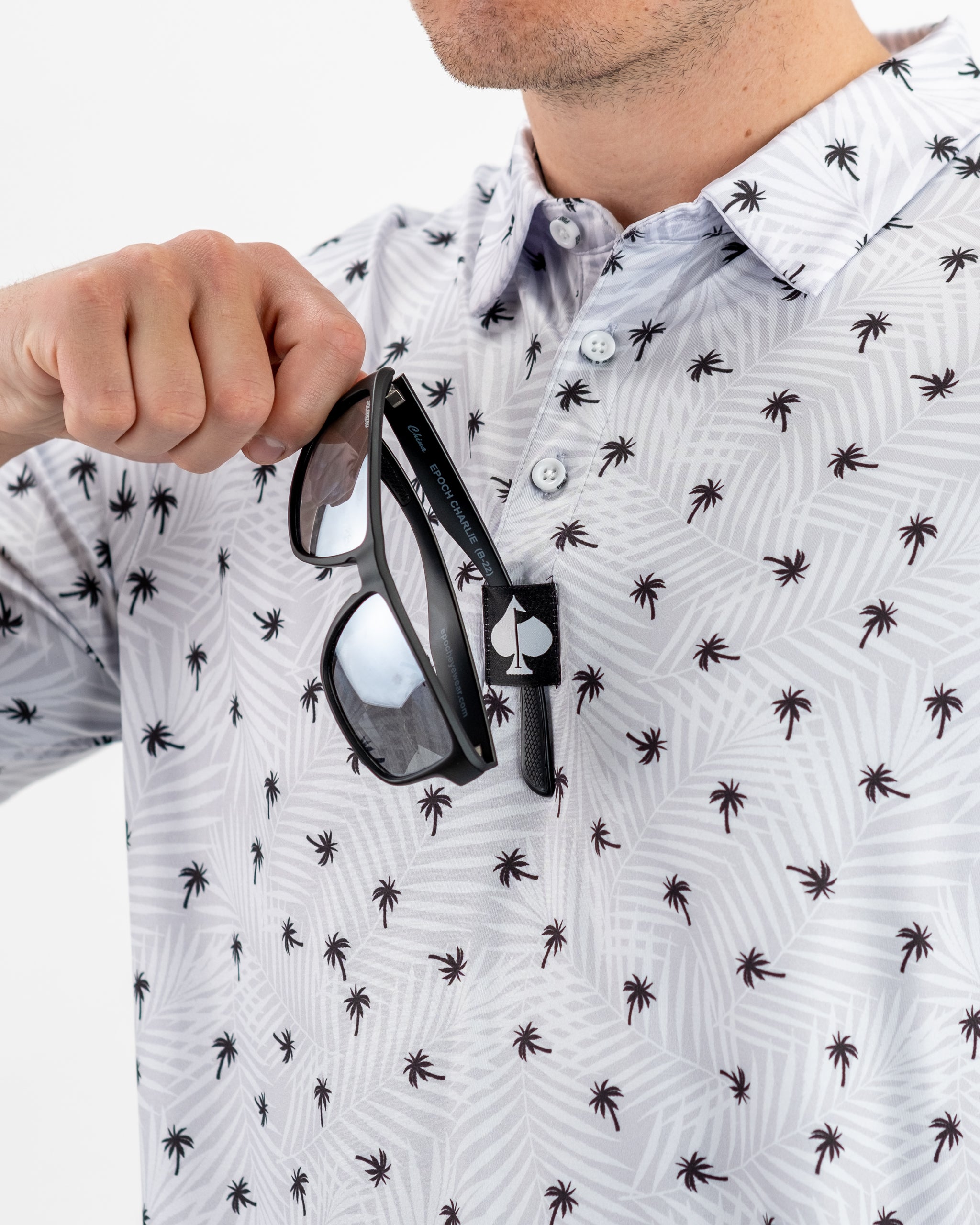Men's golf polo featuring a palm tree pattern, with sunglasses held in the front, ideal for stylish golfers.