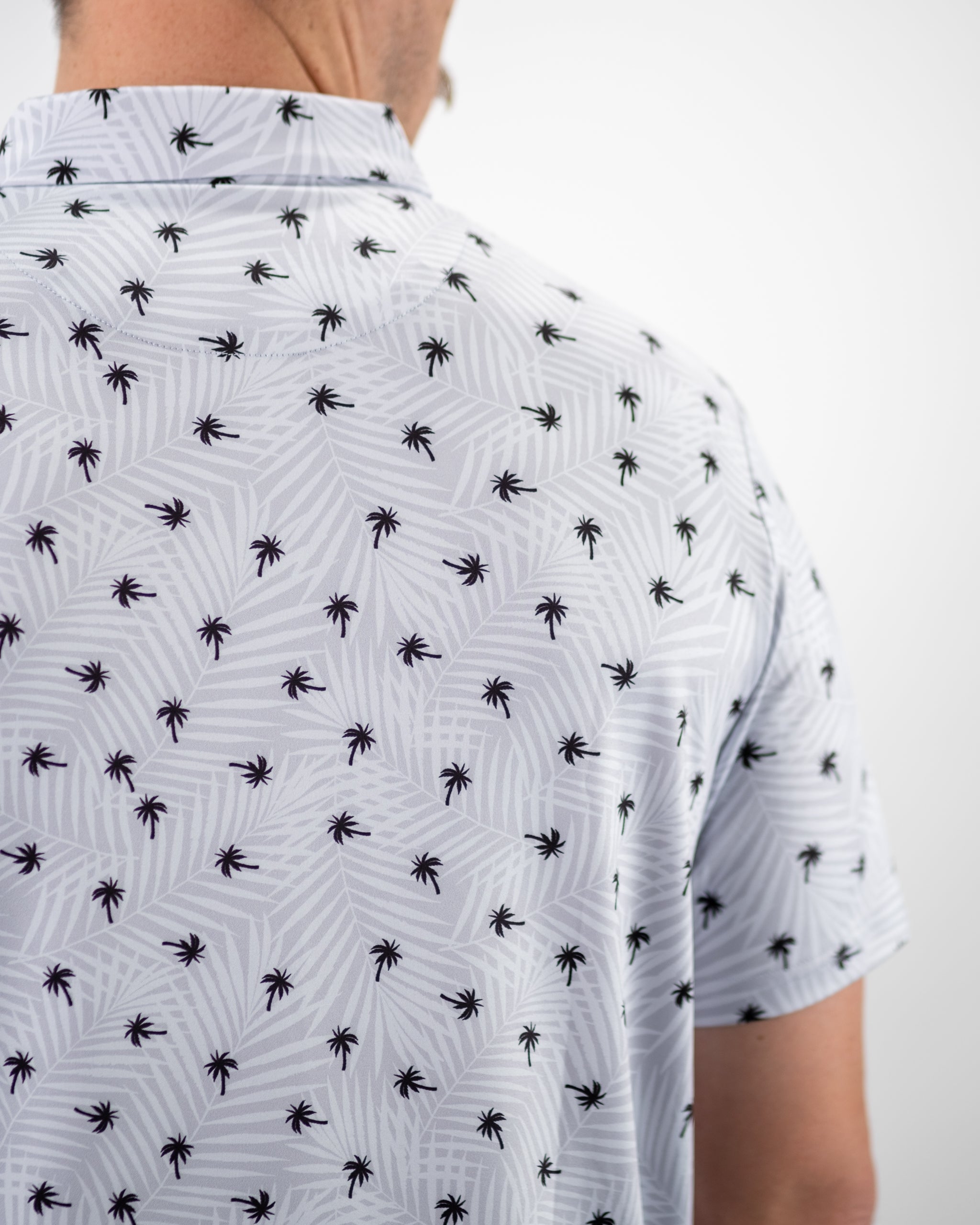 Men's golf shirt featuring a light gray background with a palm tree pattern, perfect for a stylish day on the course.