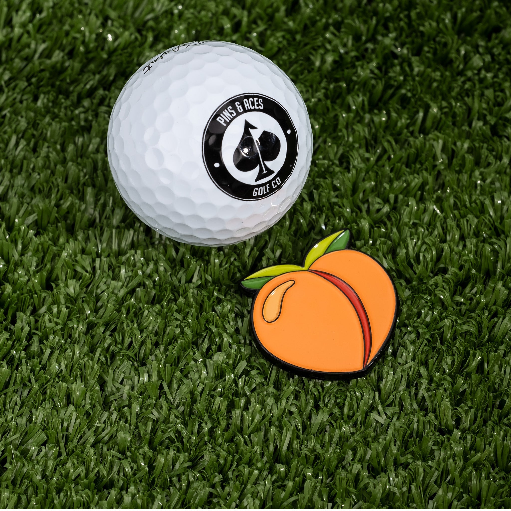 Peach-shaped ball marker next to a golf ball on green turf, perfect for adding style to your golf game.