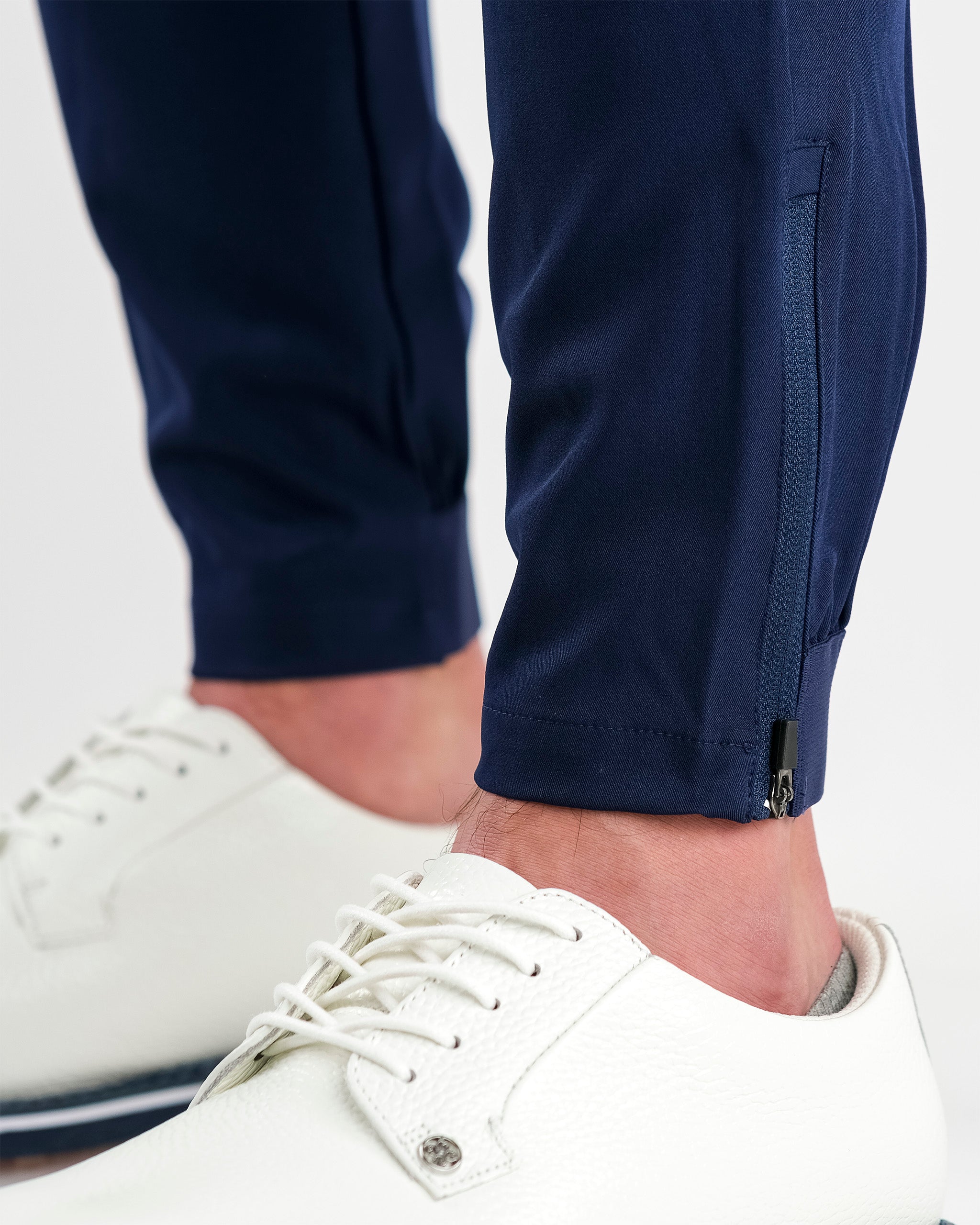 Navy performance jogger featuring a sleek design and zippered ankle detail, paired with stylish white golf shoes.
