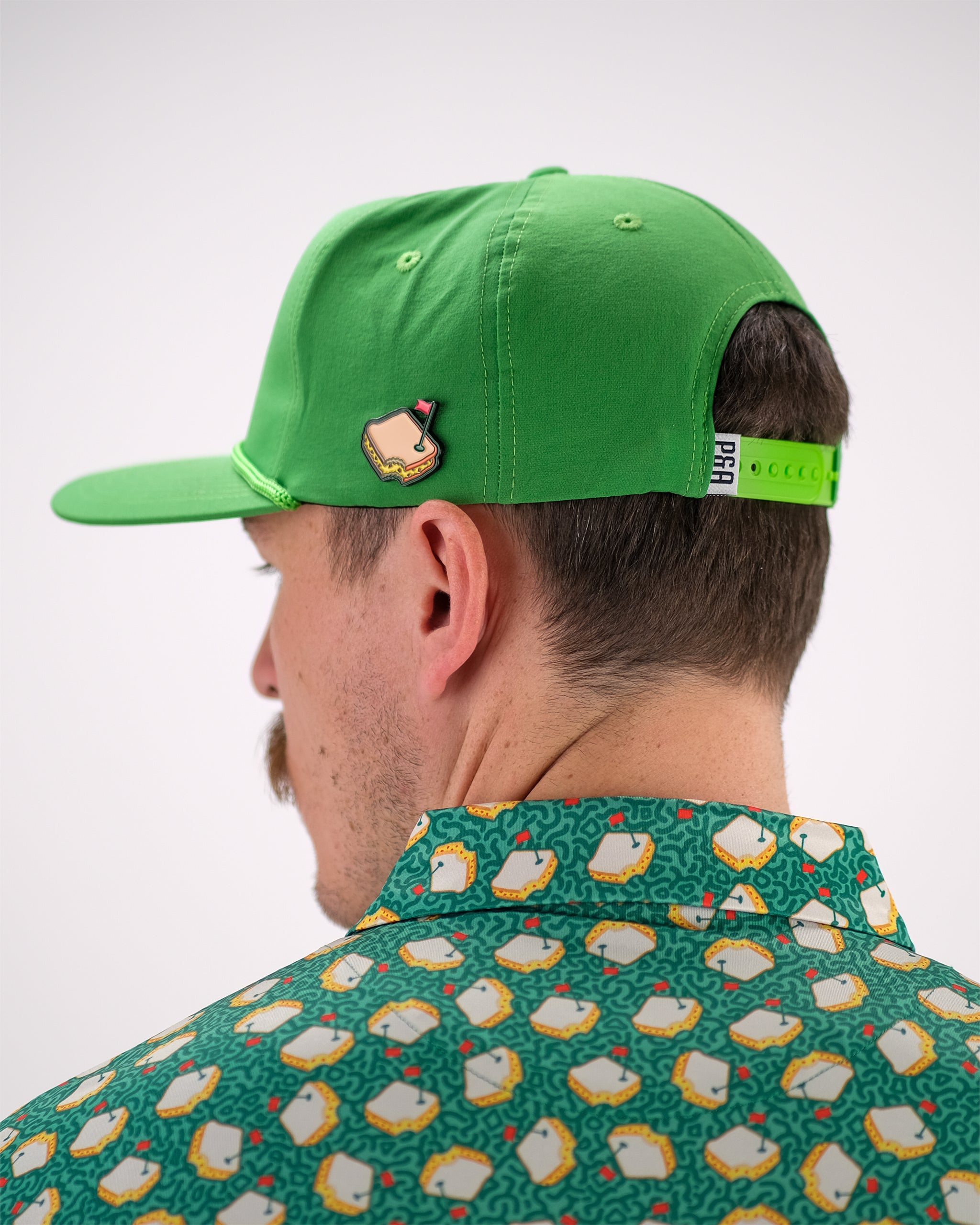 Bright green baseball cap with a golf course pin, adjustable strap, and bold golf-themed apparel for standout style on the...