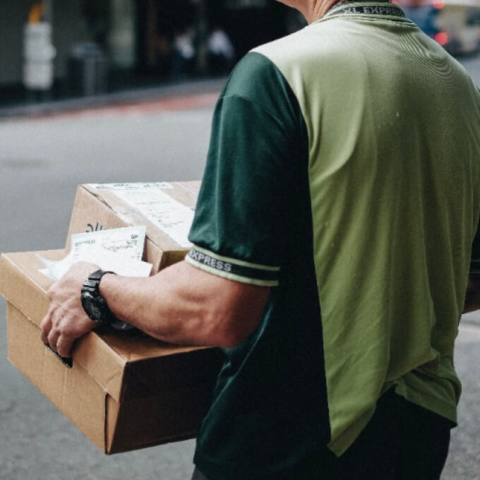 Person holding a cardboard box, wearing a lime green and dark green golf shirt with bold branding, on a city street.