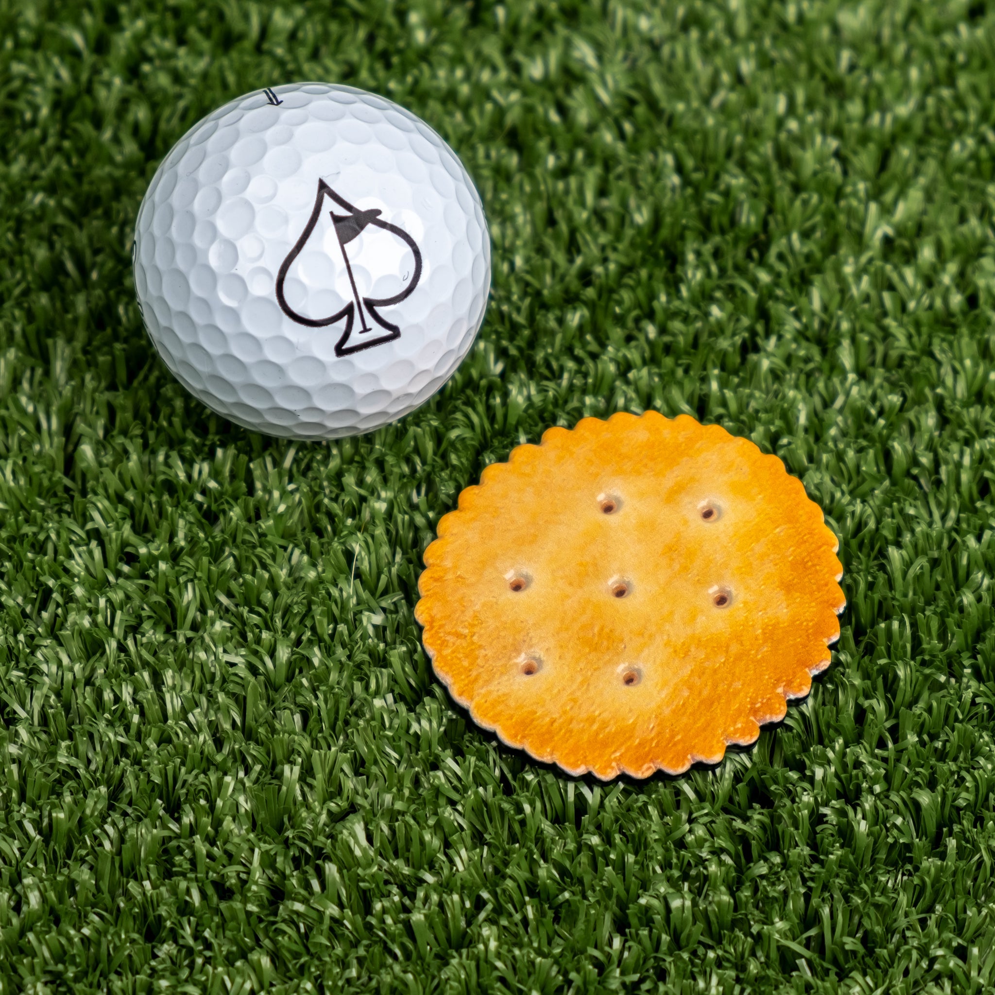 Bold golf ball marker shaped like a cracker, featuring a vibrant orange color and realistic cracker details, on green turf.
