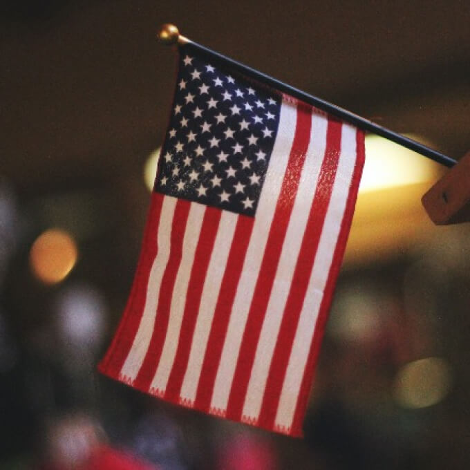Small American flag on a wooden stick, featuring bold red, white, and blue colors with stars and stripes.