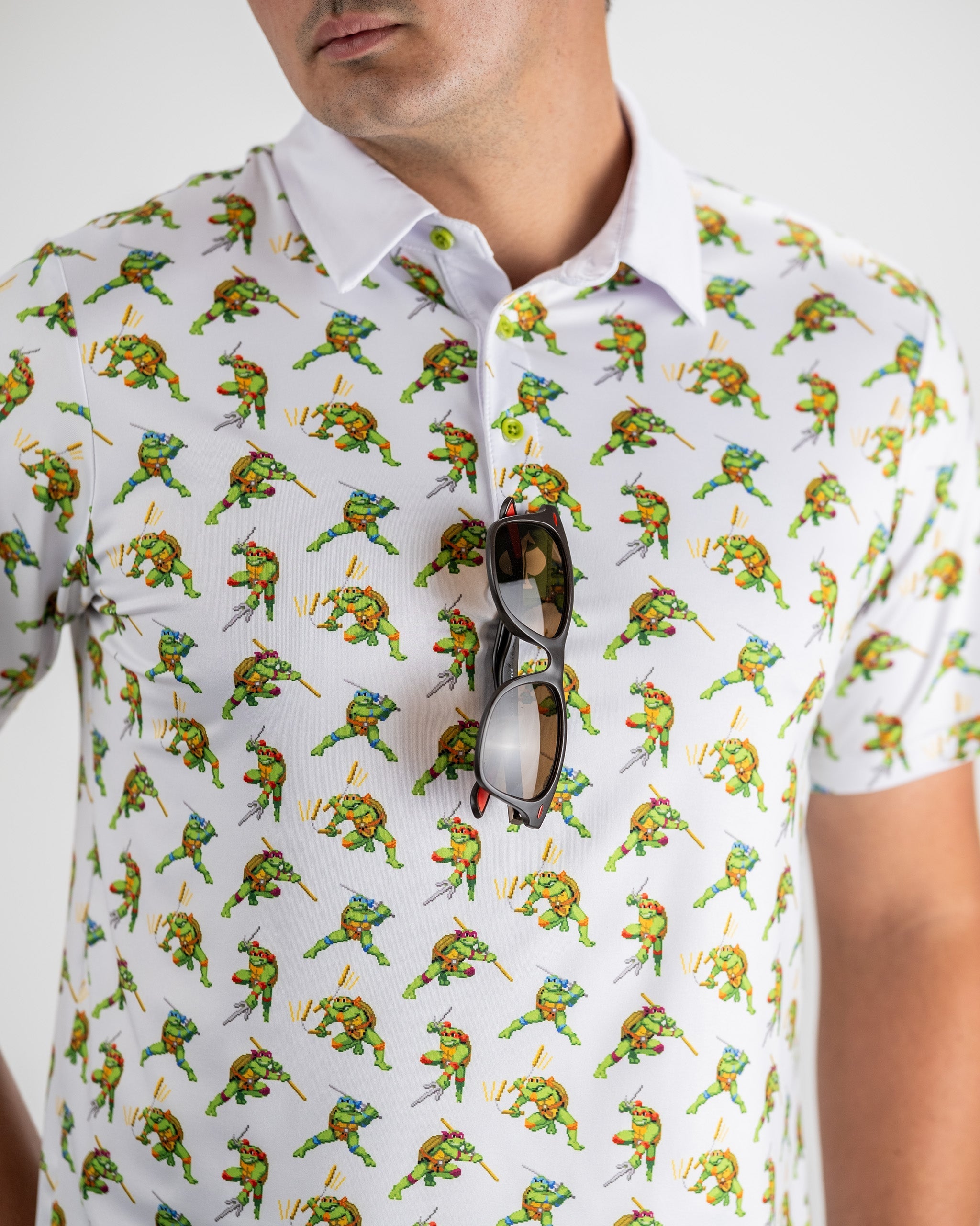 Men's golf shirt featuring an all-over 8-bit Teenage Mutant Ninja Turtles design, paired with sunglasses for a stylish look.