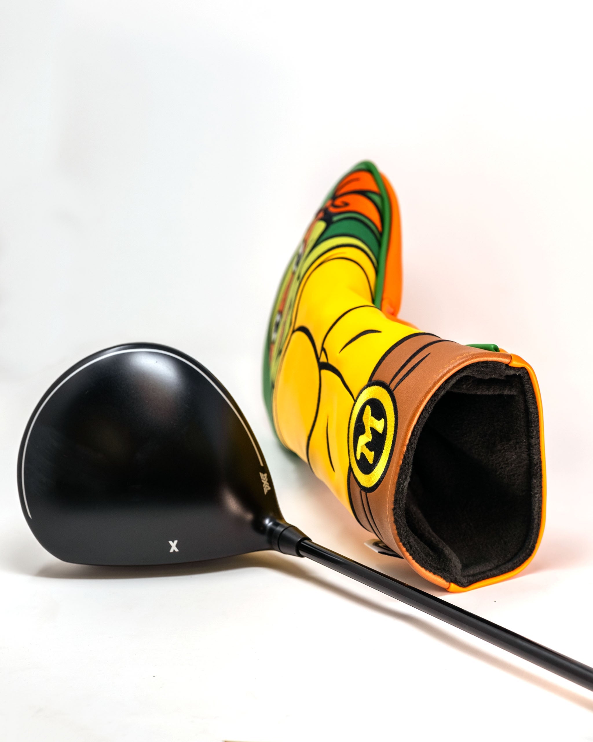 Michelangelo-themed driver cover featuring vibrant colors and character design, alongside a black golf driver.