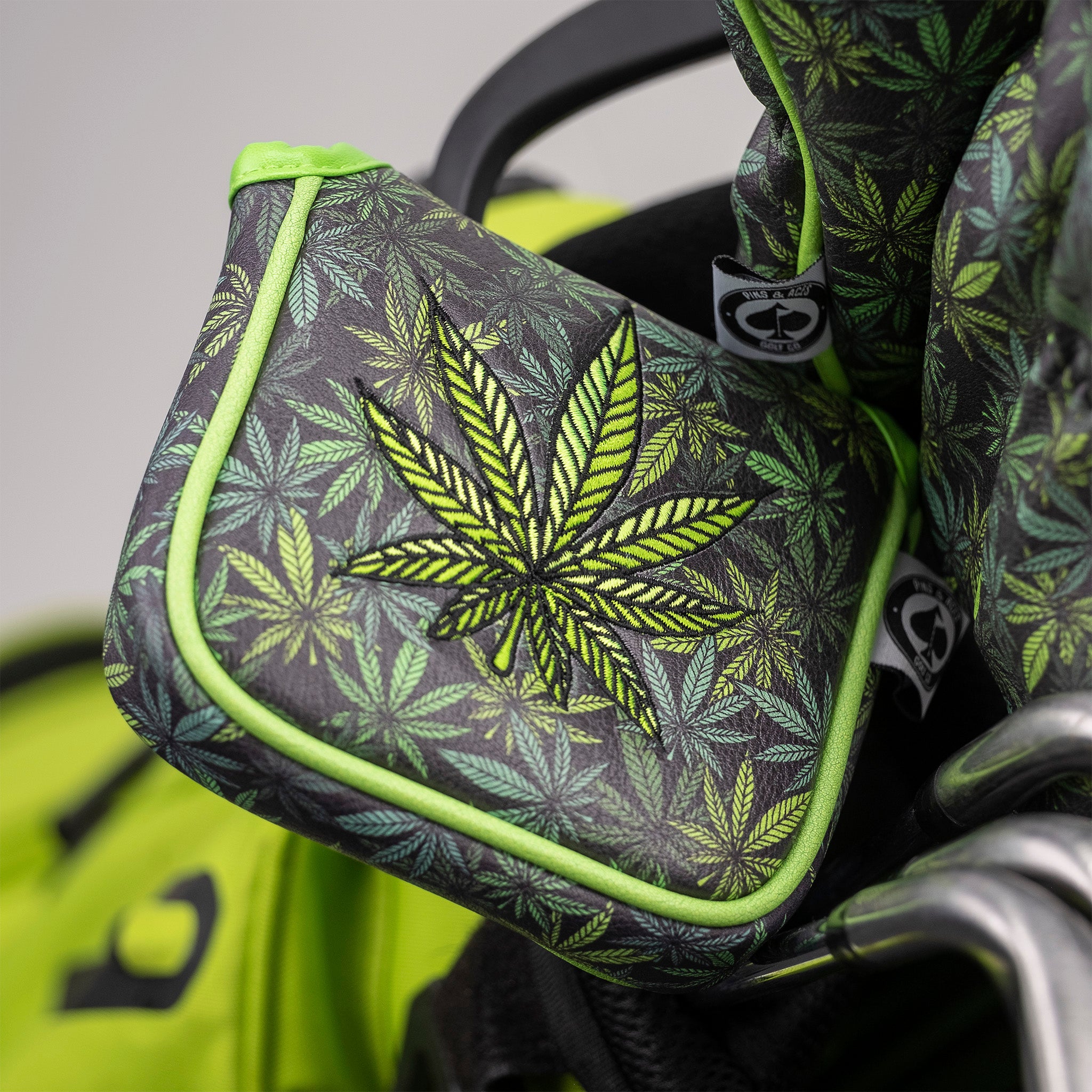 Golf headcover with neon green and black marijuana leaf pattern, accented with bright green trim, on a golf bag.