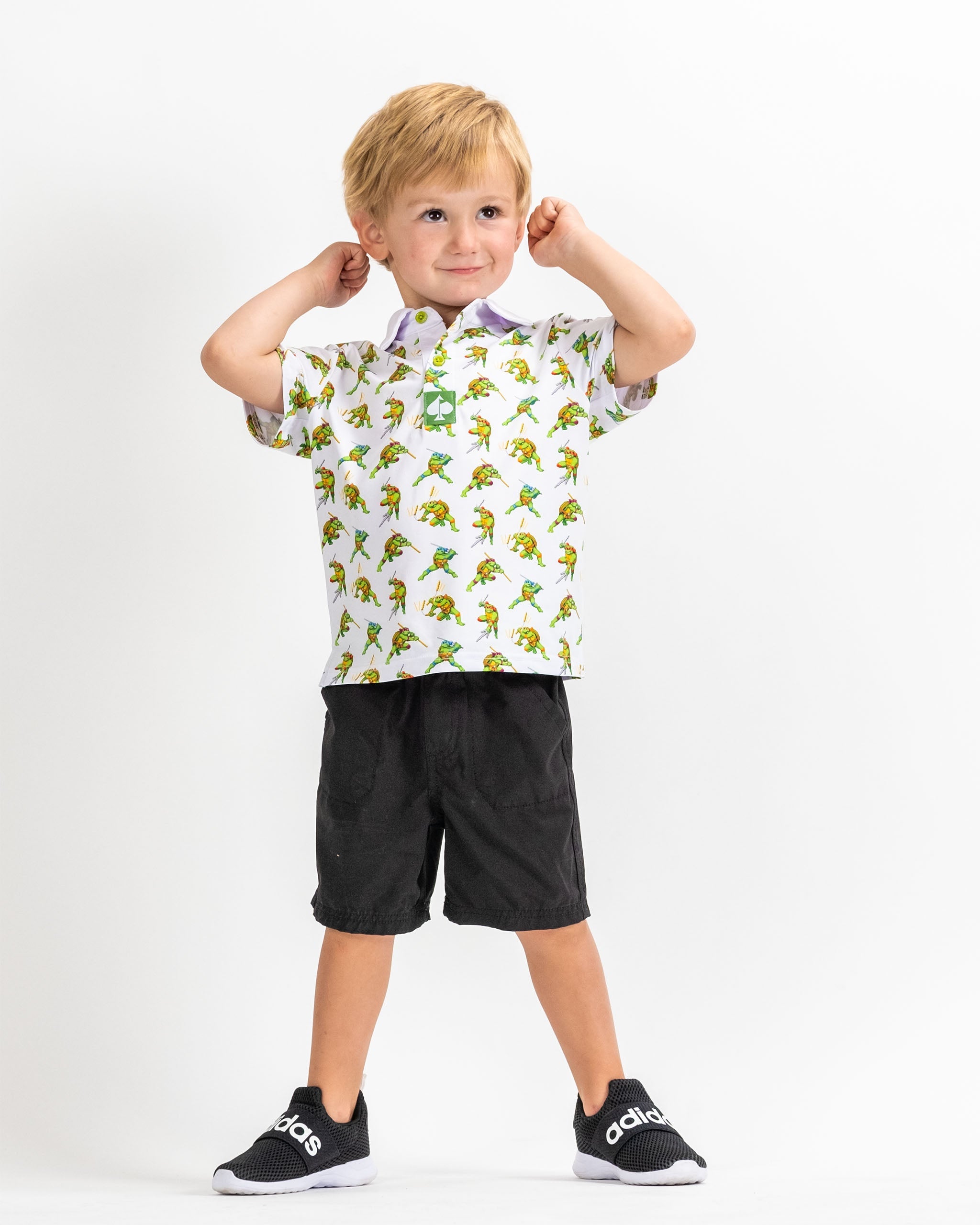 Youth wearing a TMNT Cowabunga Classic 8-Bit polo shirt featuring colorful turtle graphics, paired with black shorts.