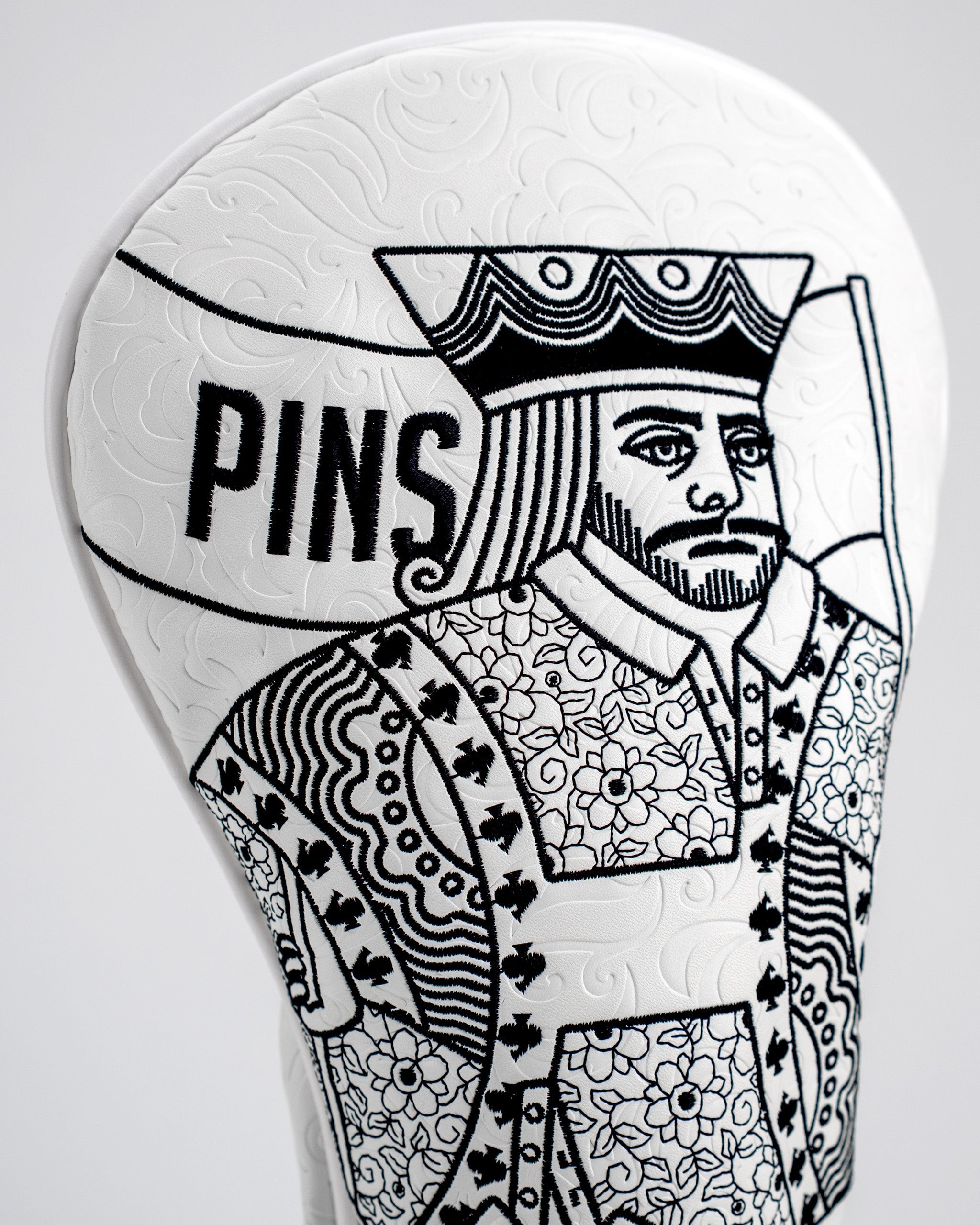 White driver cover featuring a detailed King of Spades design with floral patterns and the word "PINS" prominently displayed.