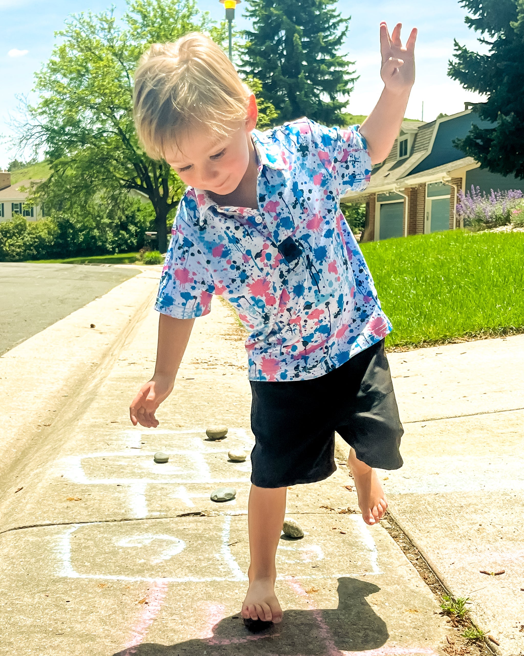 Youth Cotton Candy Drip Polo worn by a child playing hopscotch outdoors, showcasing its vibrant colors and playful design.