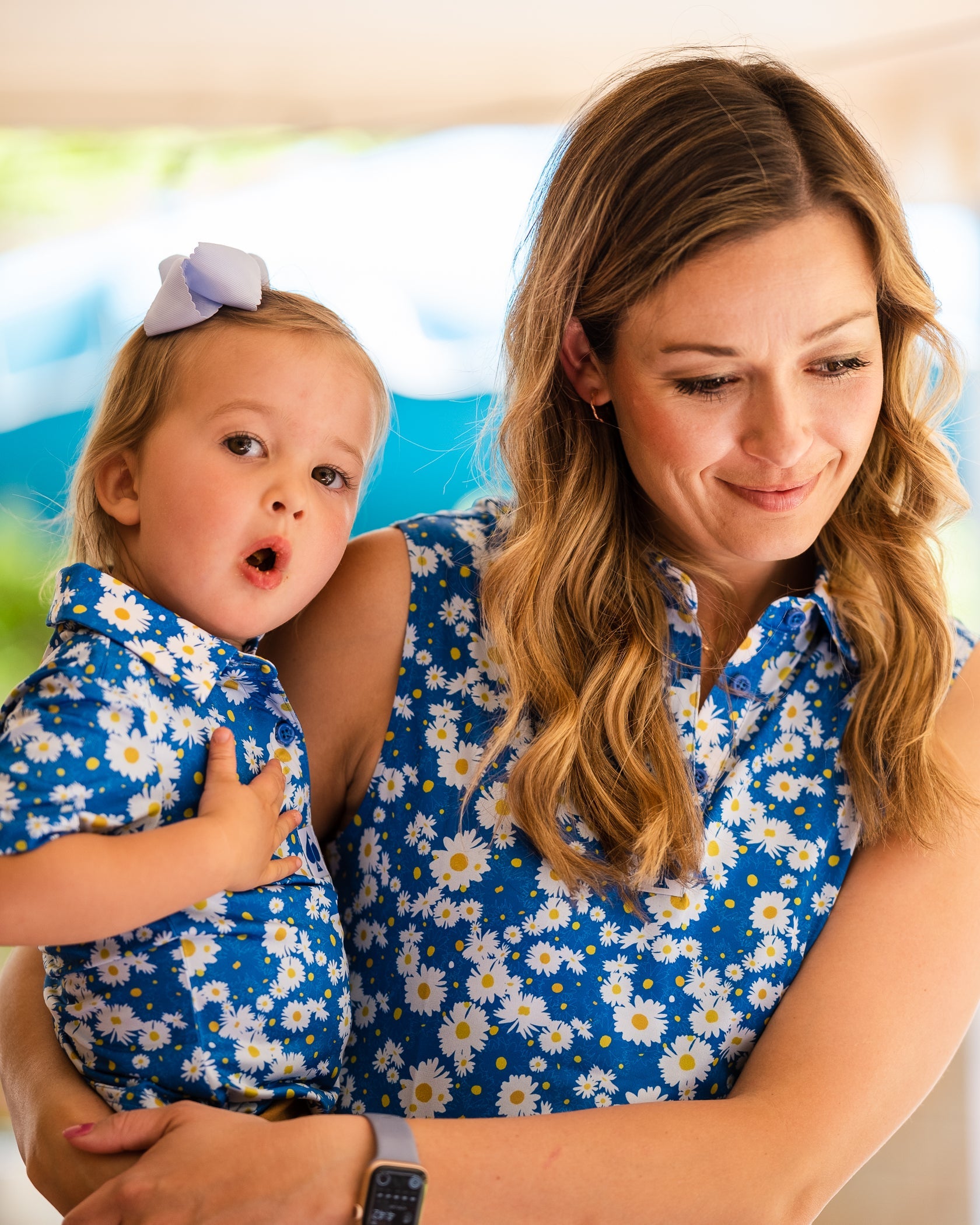 A mother holds her daughter, both wearing matching blue polos with a daisy print, showcasing a fun and stylish look.