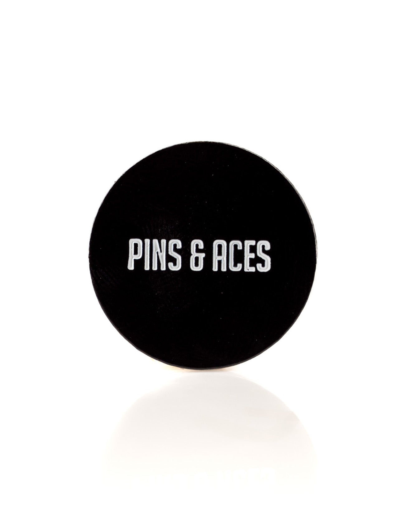 Black ball marker featuring the text "PINS & ACES" in bold white letters, designed for stylish golfers.