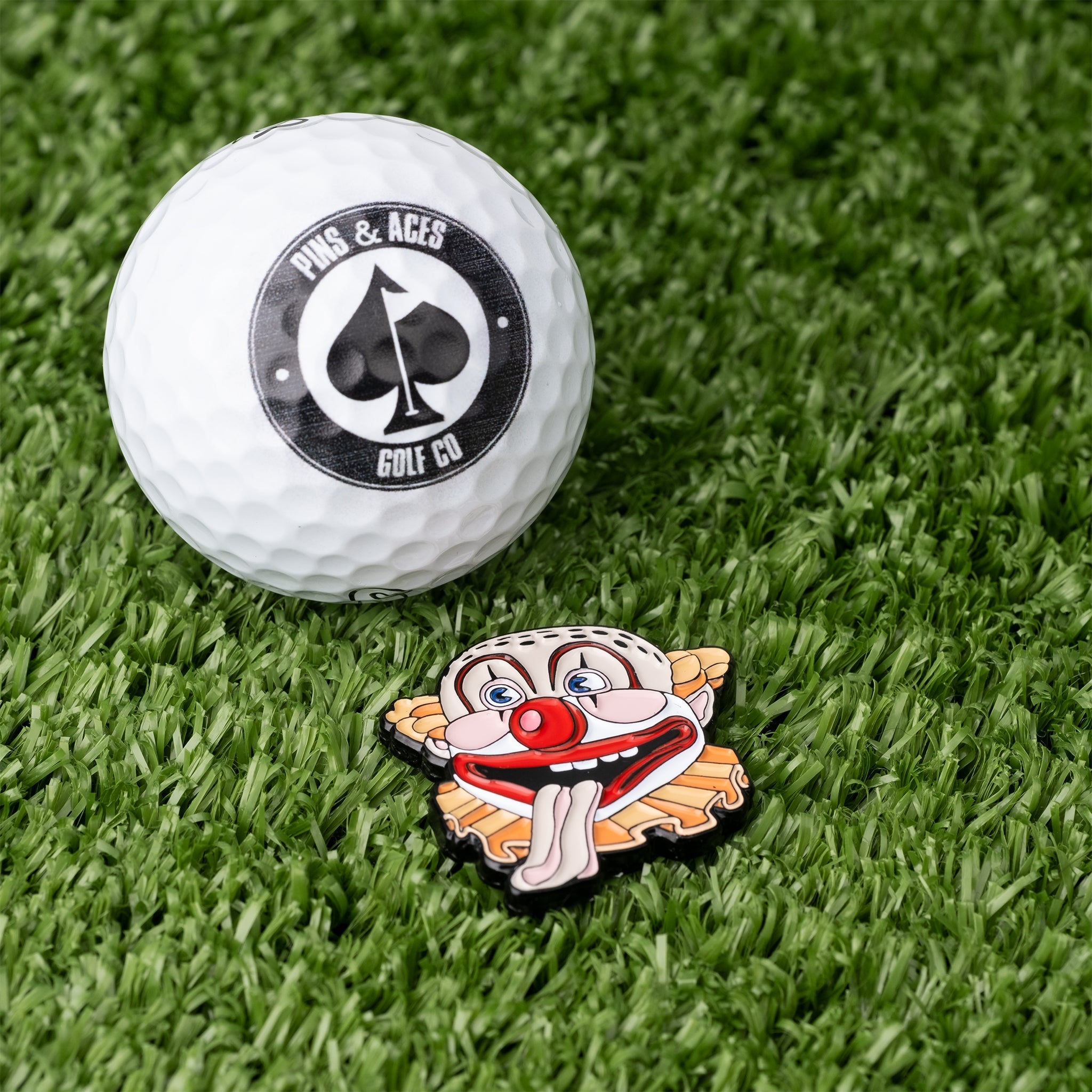 Clowns Mouth Ball Marker featuring a colorful clown design next to a golf ball with a logo on a grassy surface.