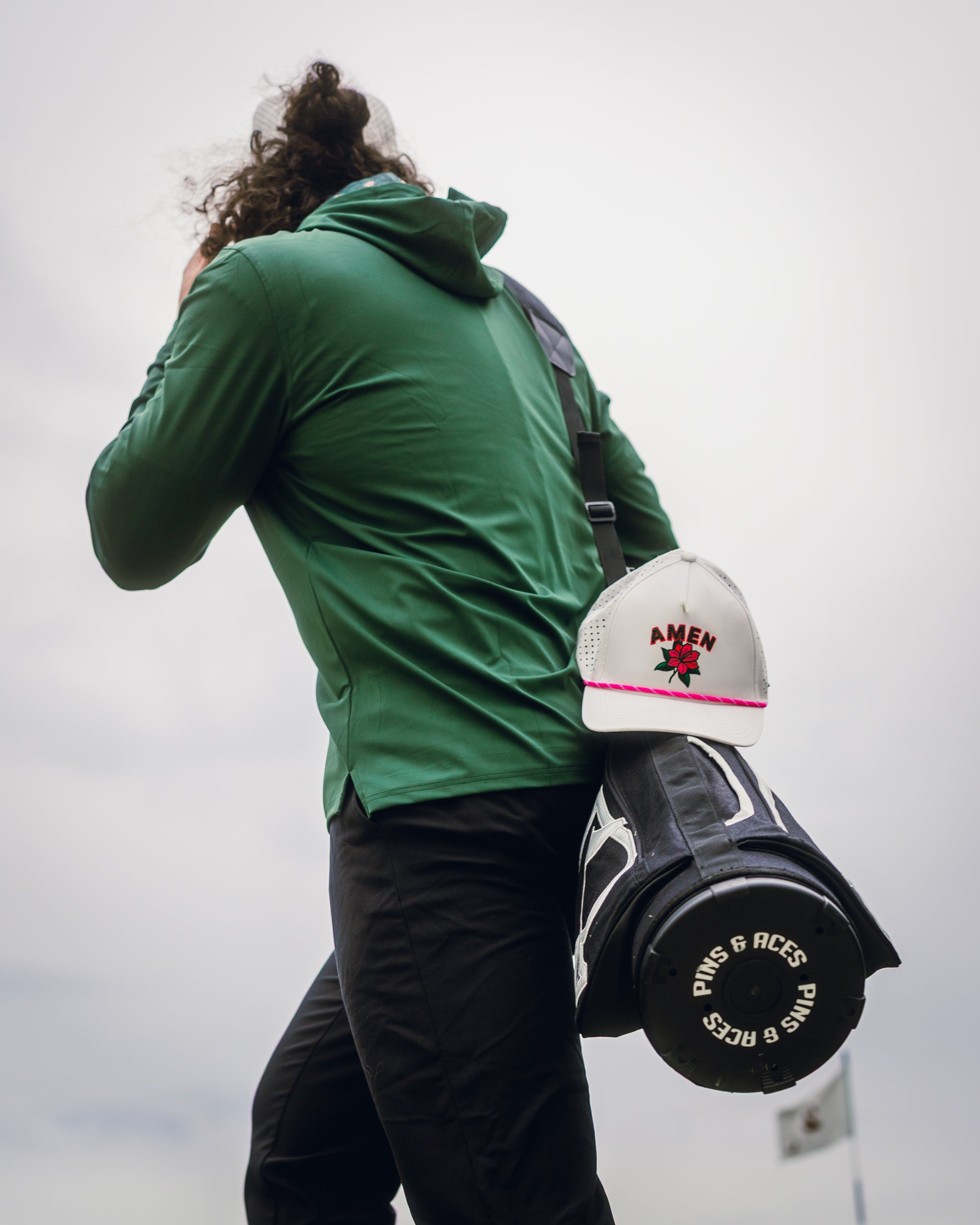 Performance golf hoodie in dark azalea, worn by a golfer carrying a golf bag and hat, ideal for stylish play on the course.