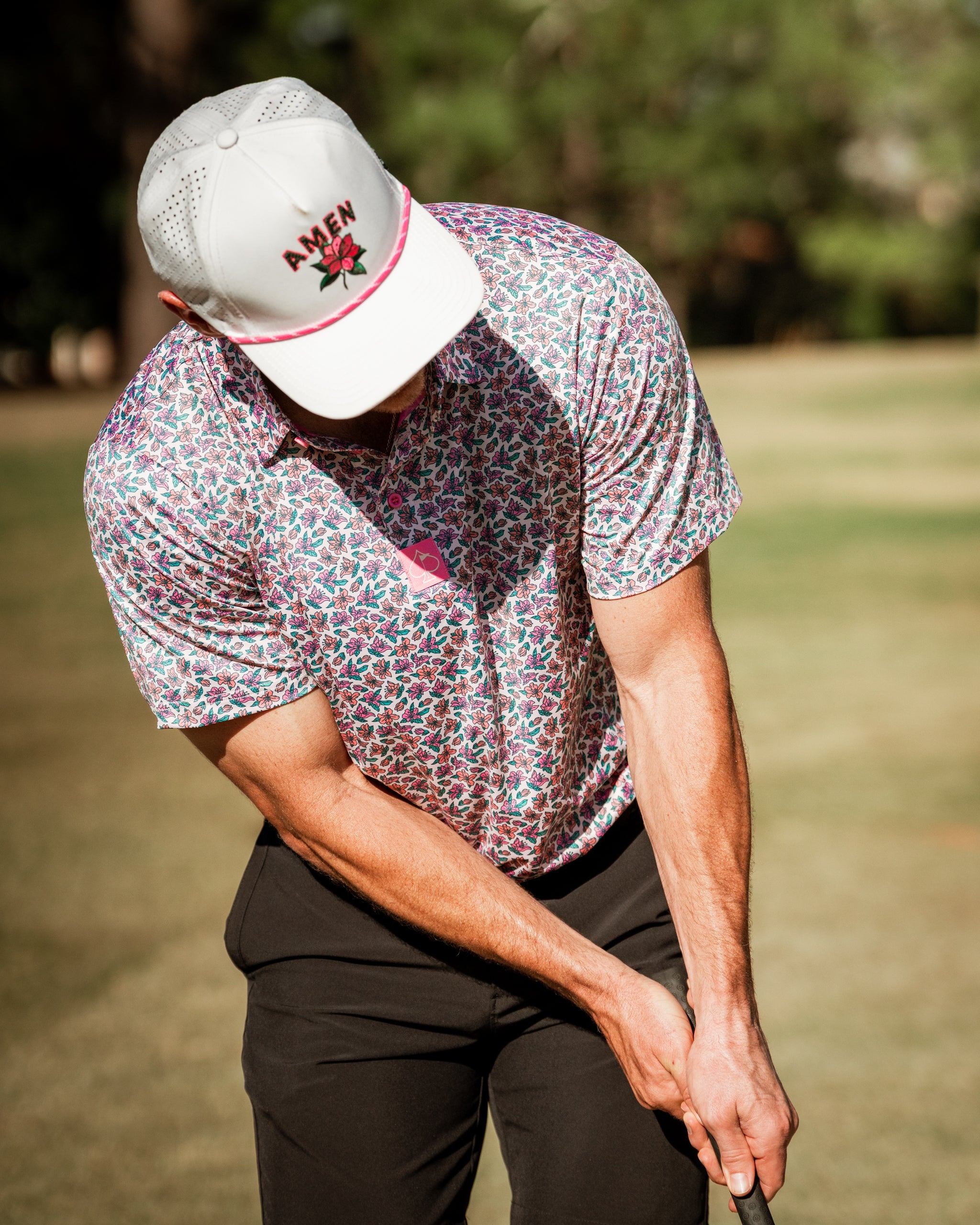 A golfer wearing a light azalea patterned shirt and a cap with "Amen" is preparing to putt on the course.