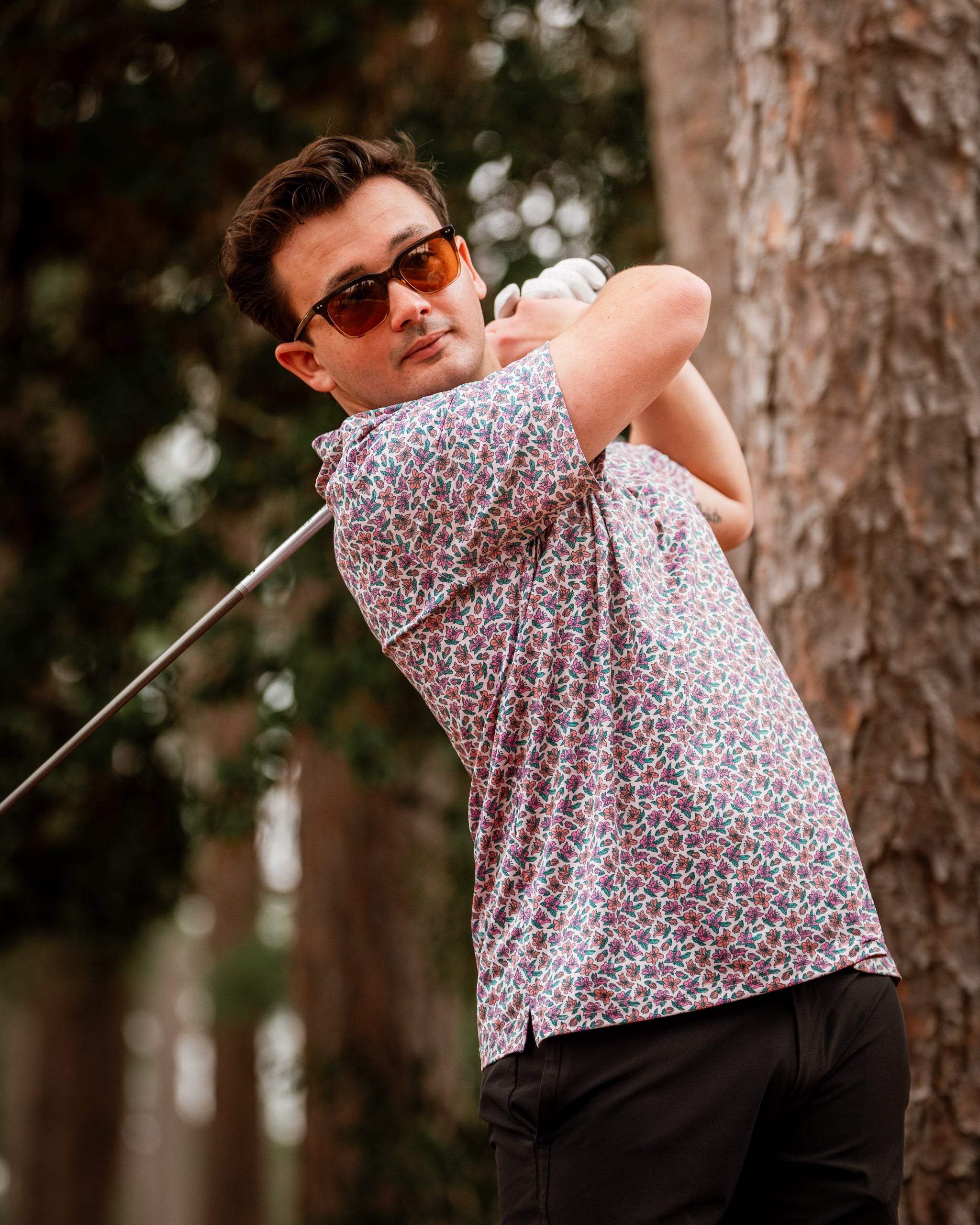 A golfer swings a club while wearing a light azalea patterned shirt, showcasing a stylish and bold golf look.