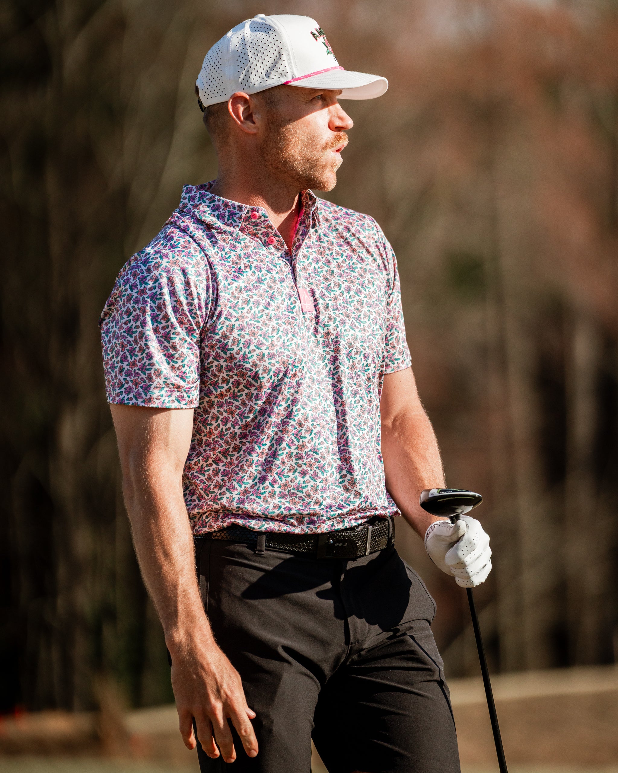 Men's Light Azalea golf polo featuring a vibrant floral pattern, paired with black pants and a white cap on the golf course.