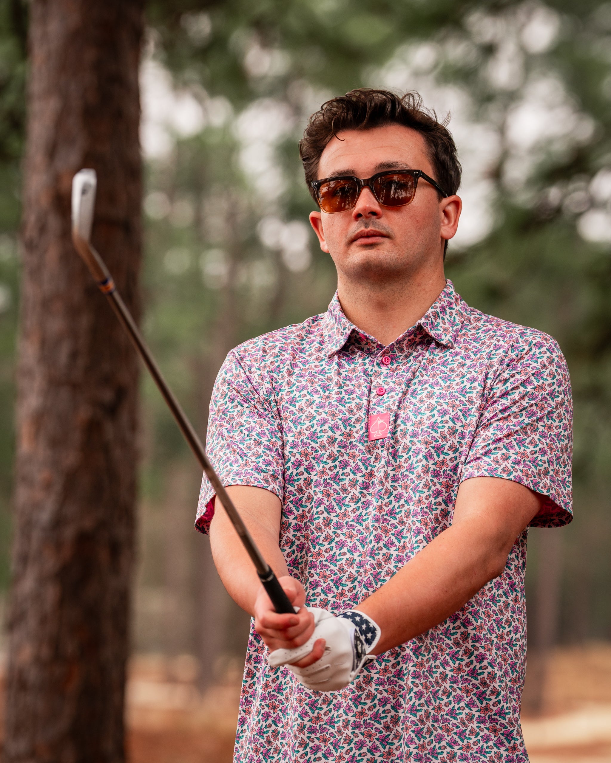 A golfer in a light azalea patterned shirt prepares to swing on a tree-lined course, showcasing bold golf fashion.