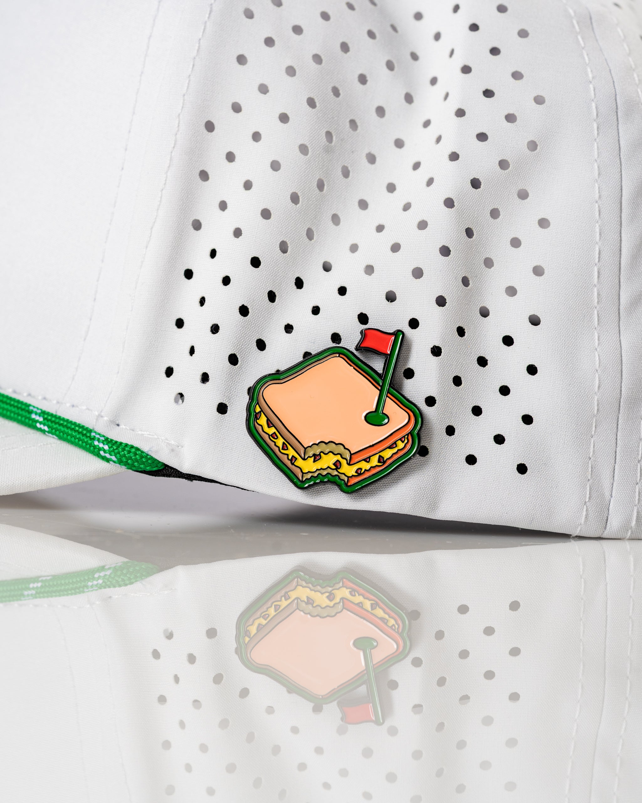 Perforated white rope hat featuring a colorful pimento cheese sandwich pin, ideal for stylish golfers.