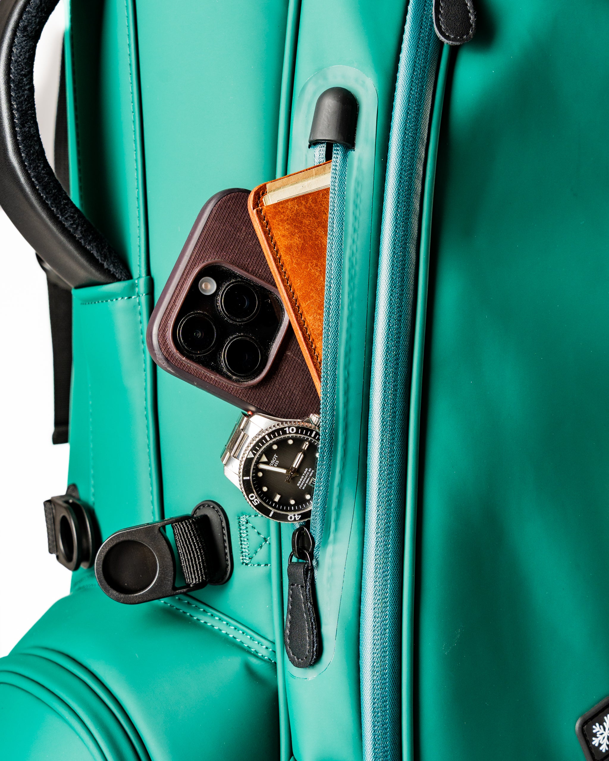Close-up of a teal golf bag featuring a phone, wallet, and watch in the front pocket, showcasing functional design.