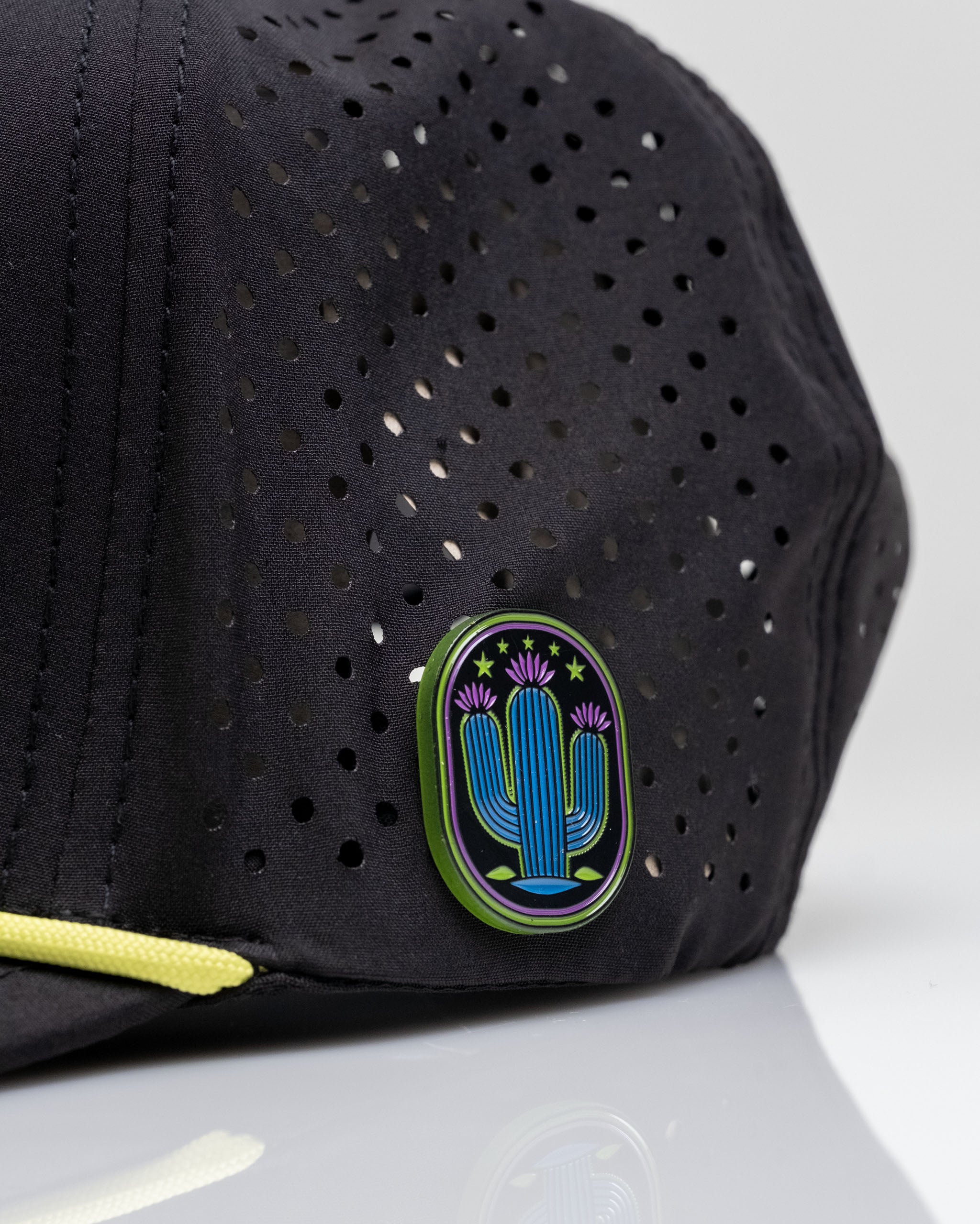 Perforated black rope hat featuring a colorful cactus logo, designed for stylish golfers seeking unique accessories.