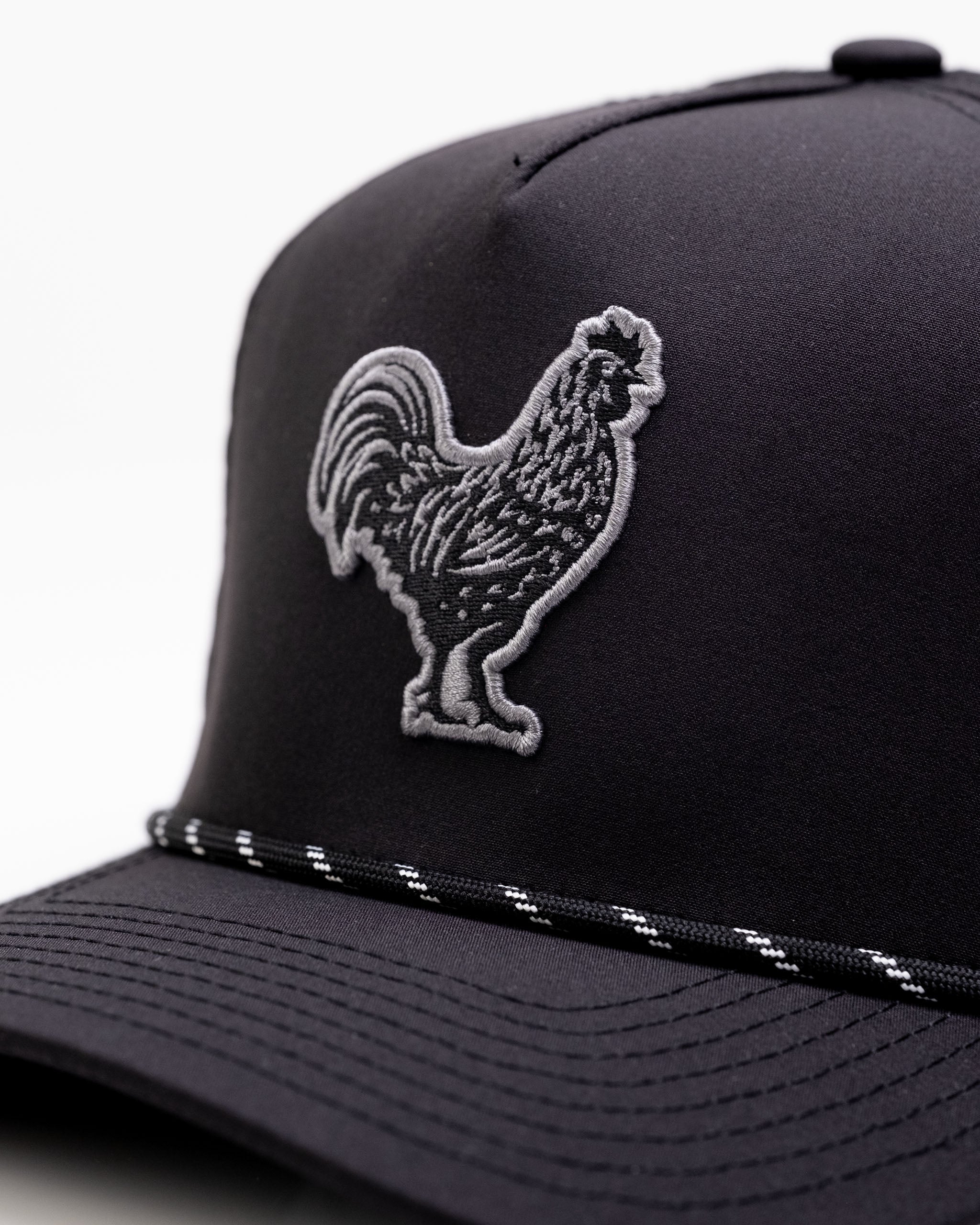 Black perforated rope hat featuring a detailed rooster emblem, designed for stylish golfers seeking standout accessories.