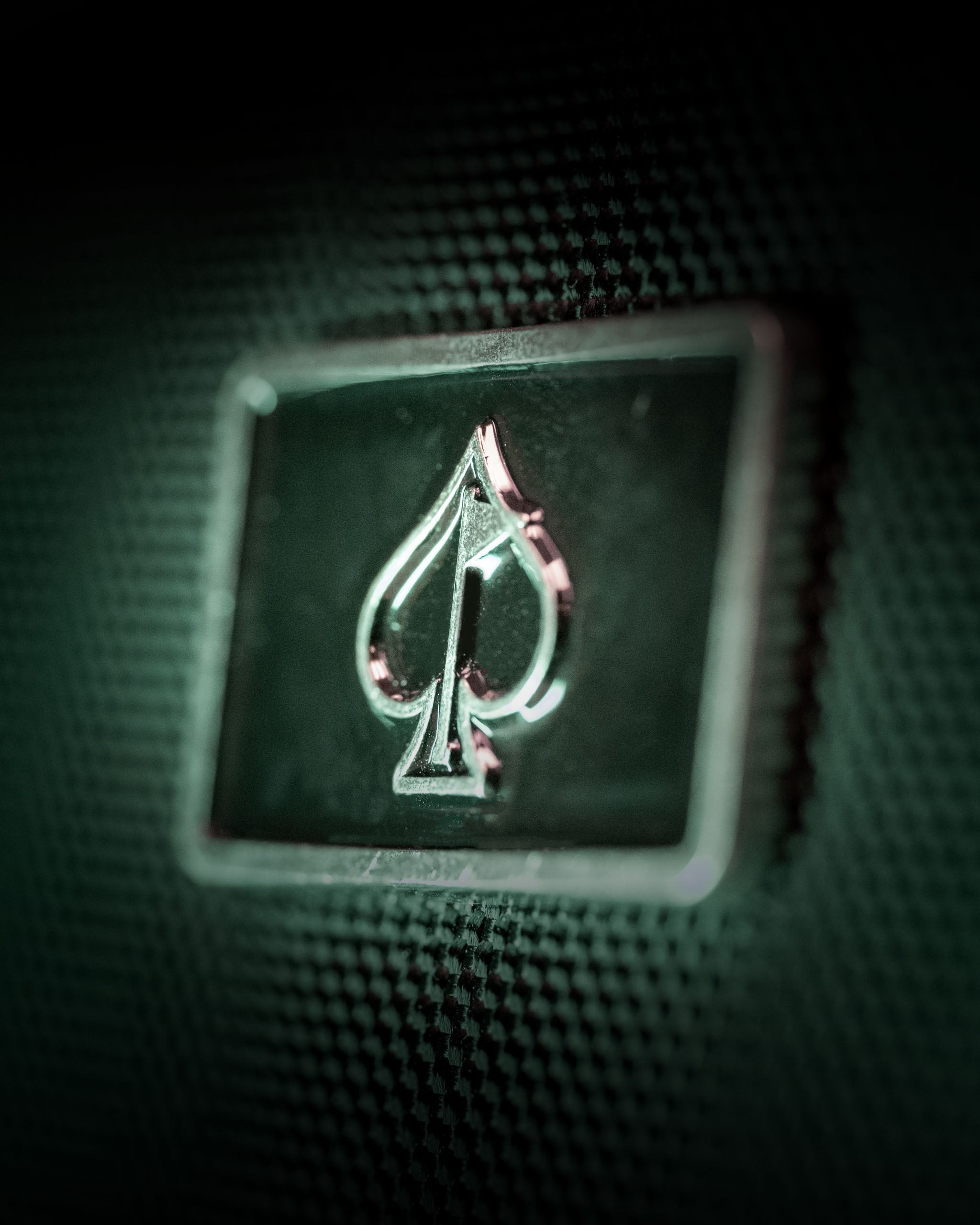 Close-up of a sleek metal logo featuring a spade design on a textured black backpack, emphasizing style and quality.