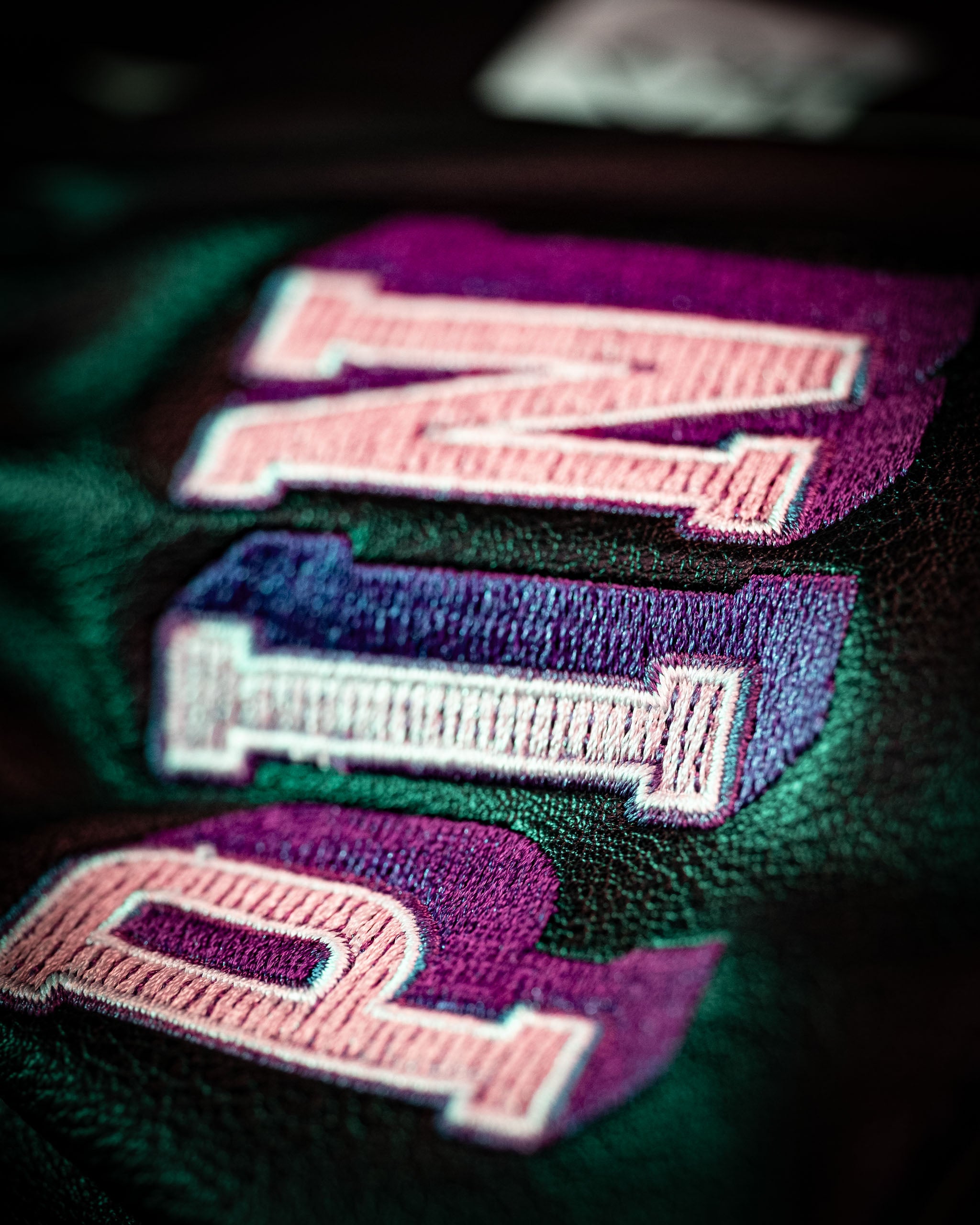 Close-up of embroidered letters on a black backpack, showcasing vibrant purple and pink colors for a bold, stylish look.
