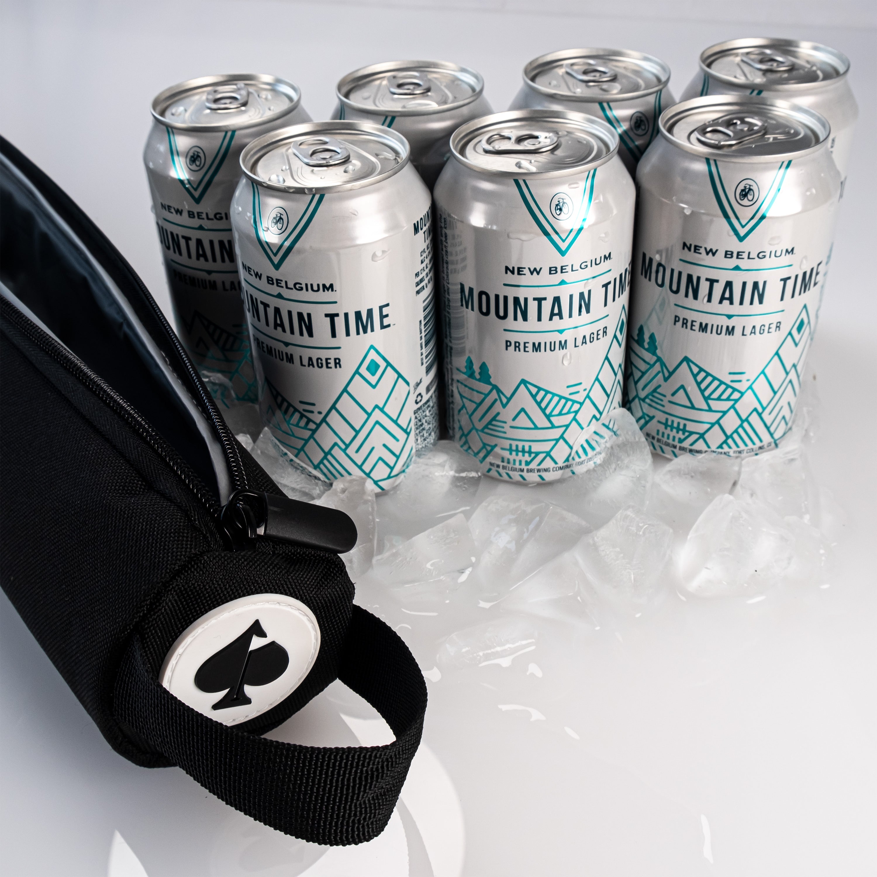 Bold mountain-themed cans of New Belgium Mountain Time lager with a black golf accessory pouch on ice.
