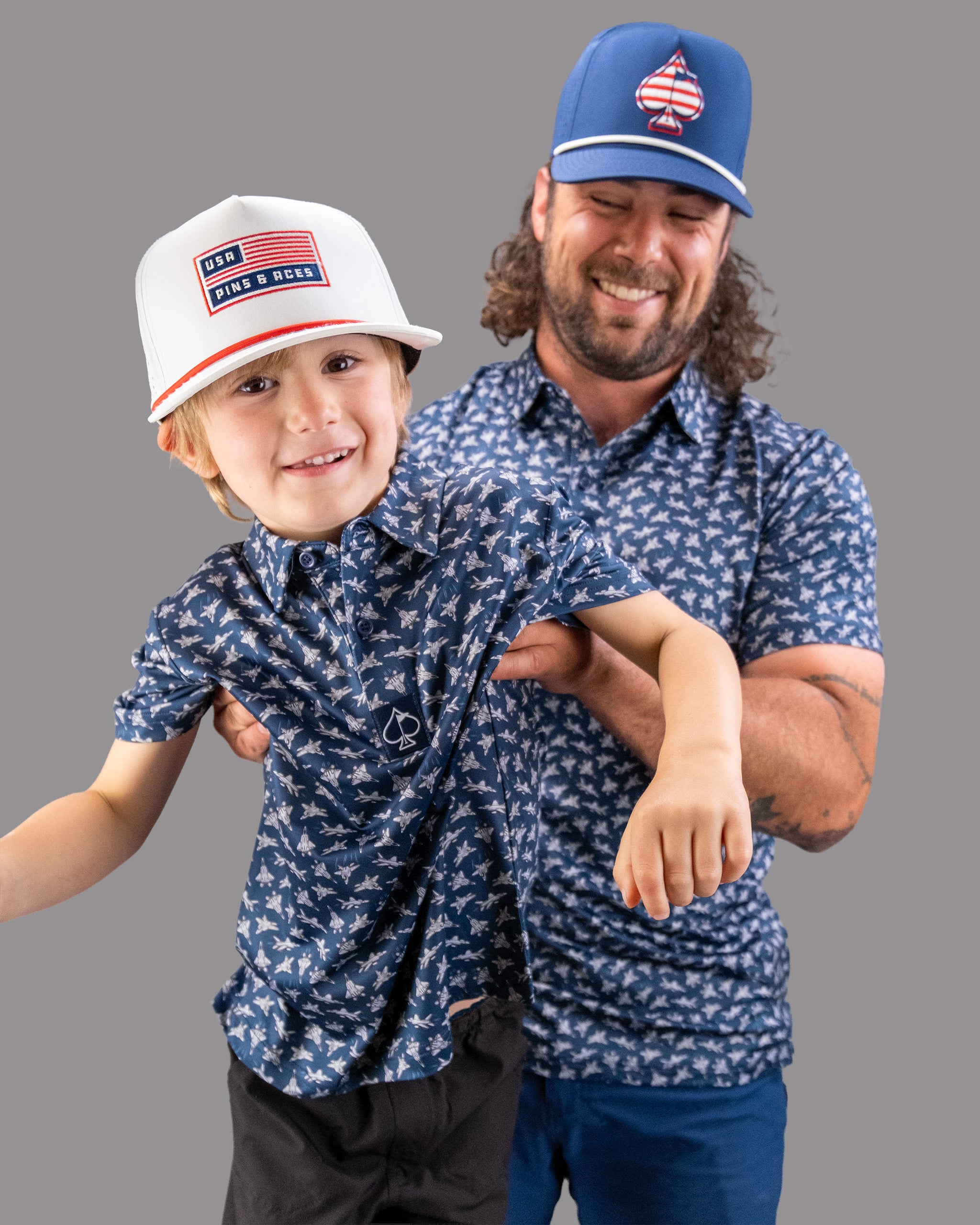 Two smiling males wearing matching navy blue shirts with white bird patterns, one adult and one child, both sporting caps.