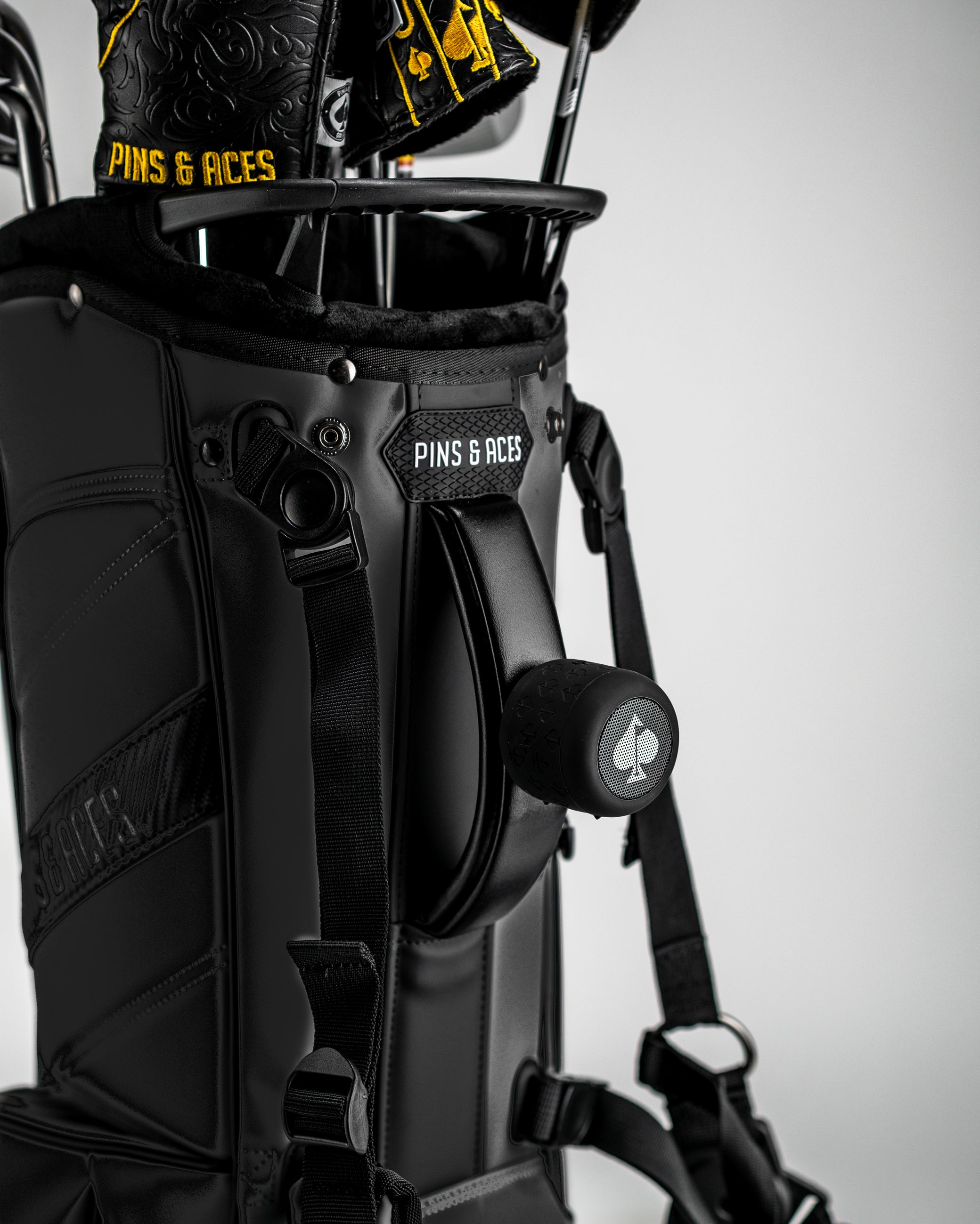 Black golf bag with "PINS & ACES" logo, featuring bold headcovers with yellow accents and golf accessories for standout st...