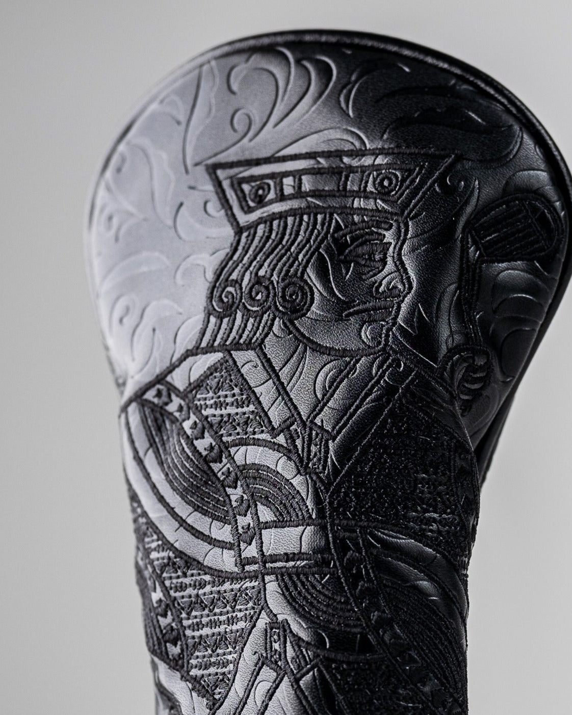 Close-up of a black golf club headcover with intricate, bold embossed tribal design, perfect for standout golf attire.