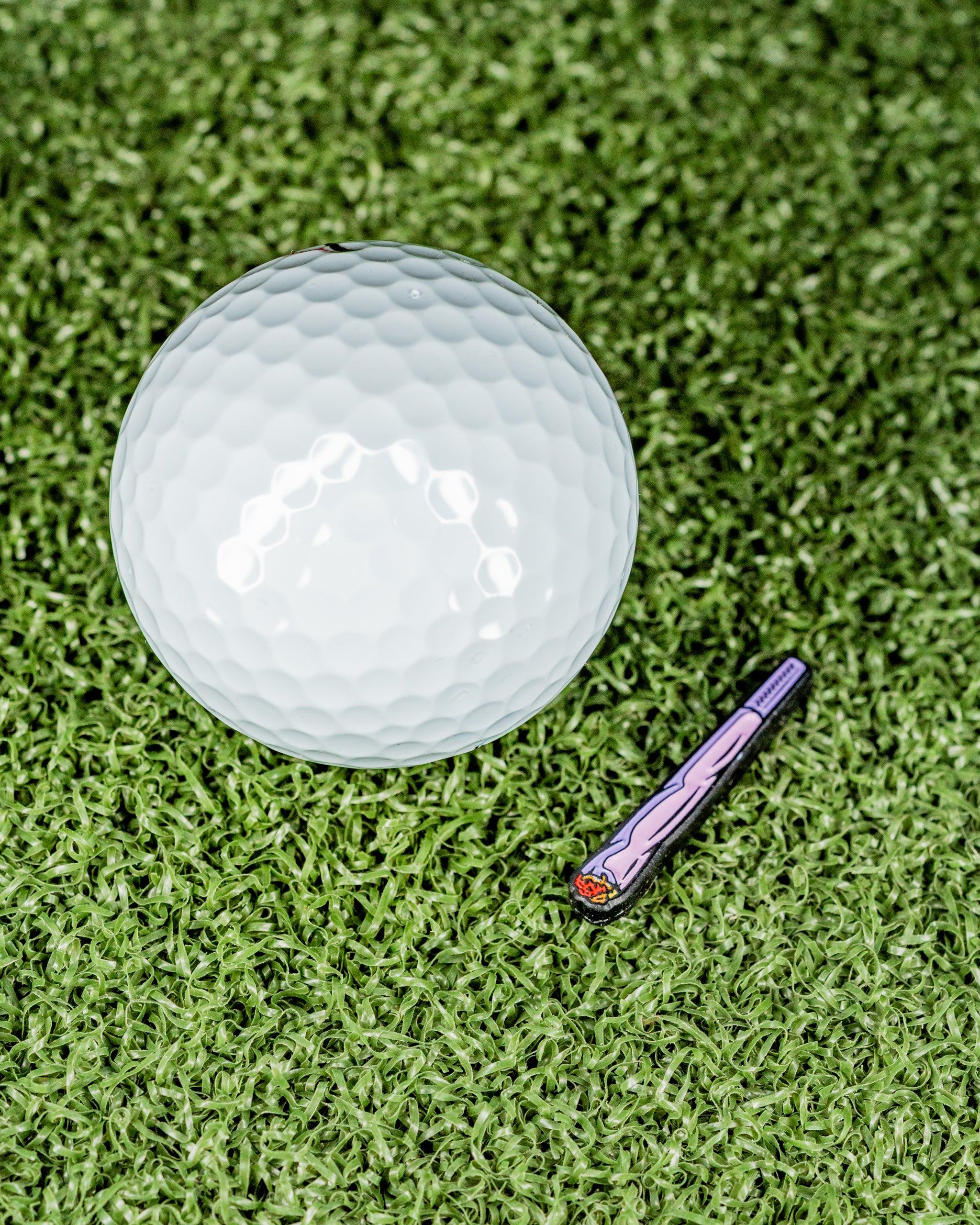 Blazy Susan Pink J ball marker beside a white golf ball on green turf, featuring a unique design for stylish play.