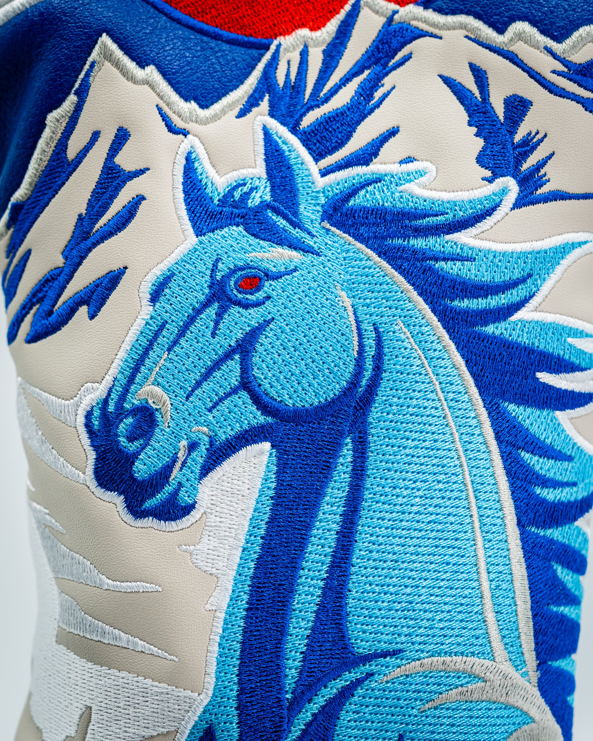 Blue embroidered horse design on a driver cover, featuring intricate details and a vibrant color palette.