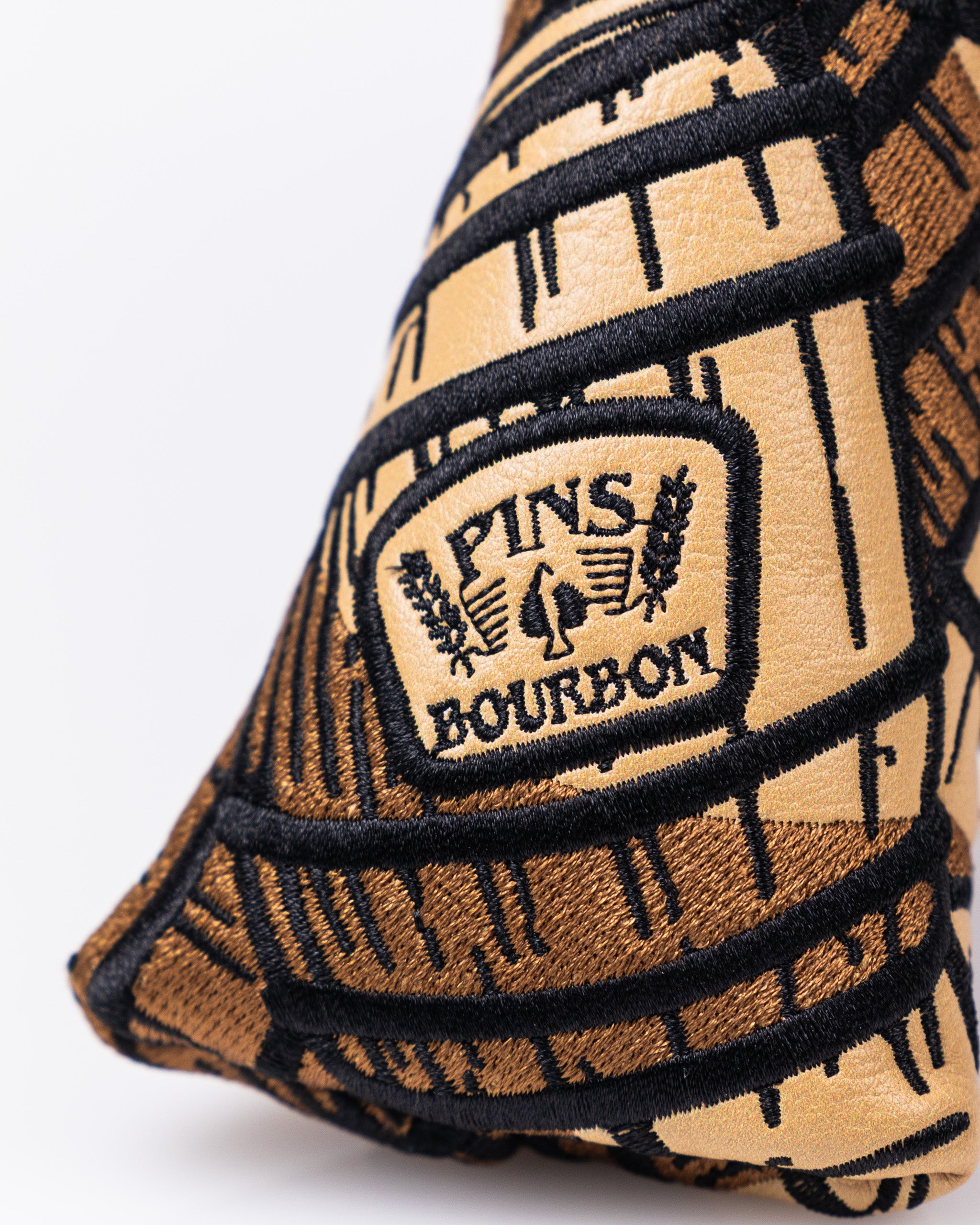 Close-up of a bold, embroidered golf headcover featuring a tan and black design with "Pins & Bourbon" logo, perfect for st...