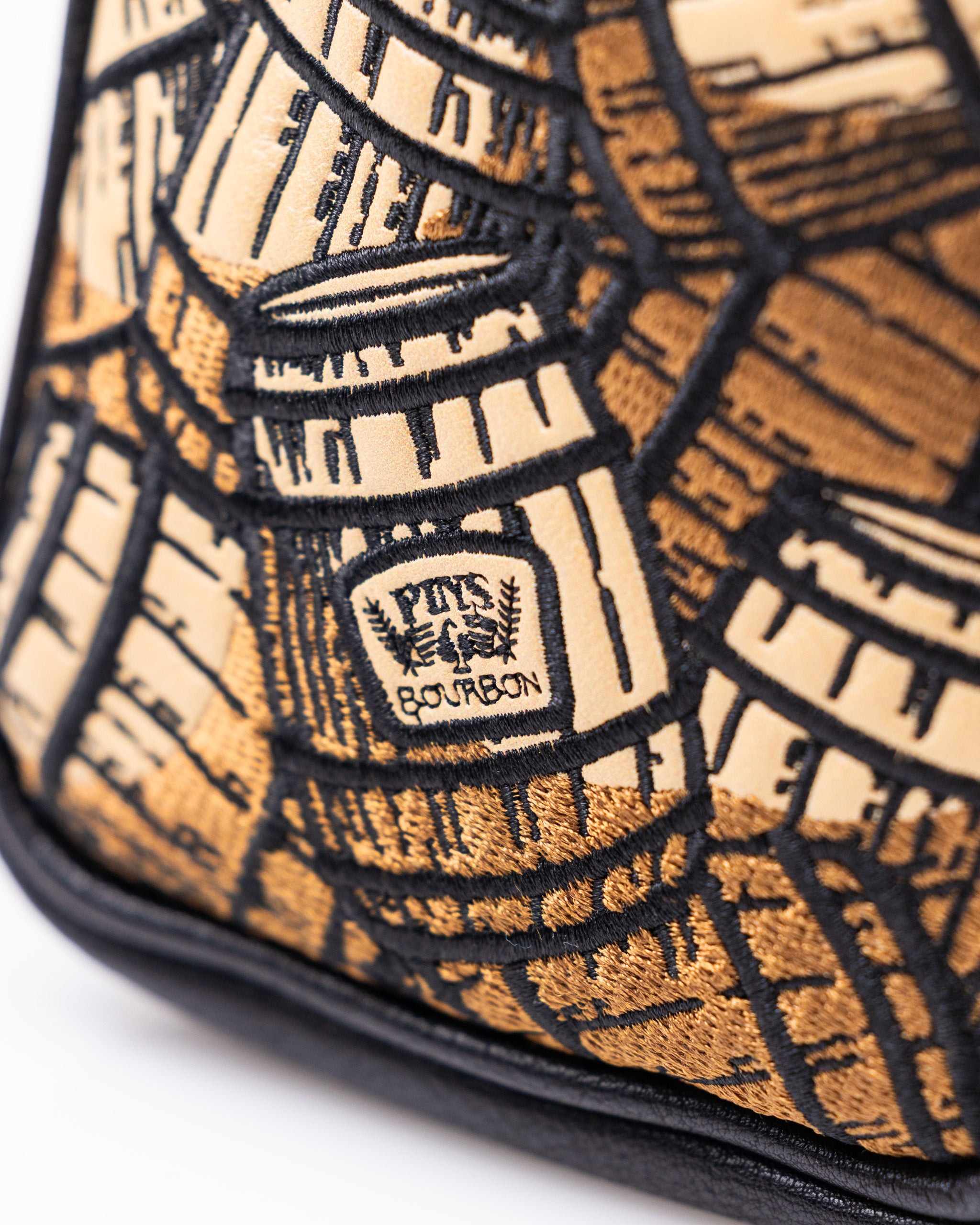 Close-up of a bold, embroidered golf headcover in tan and black, featuring the "Pits & Bourbon" logo and intricate geometr...