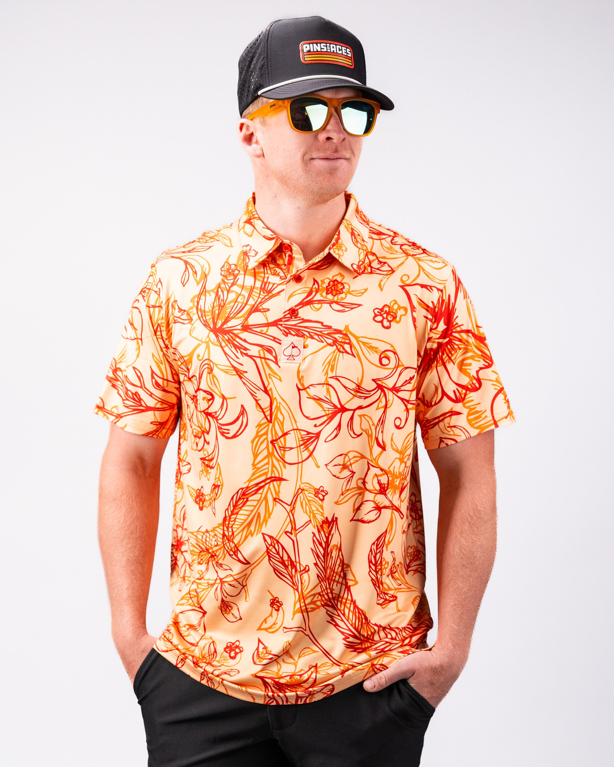Cabo Sunburst polo shirt in vibrant orange with a sunburst pattern, featuring a collar and short sleeves, displayed on a flat surface.