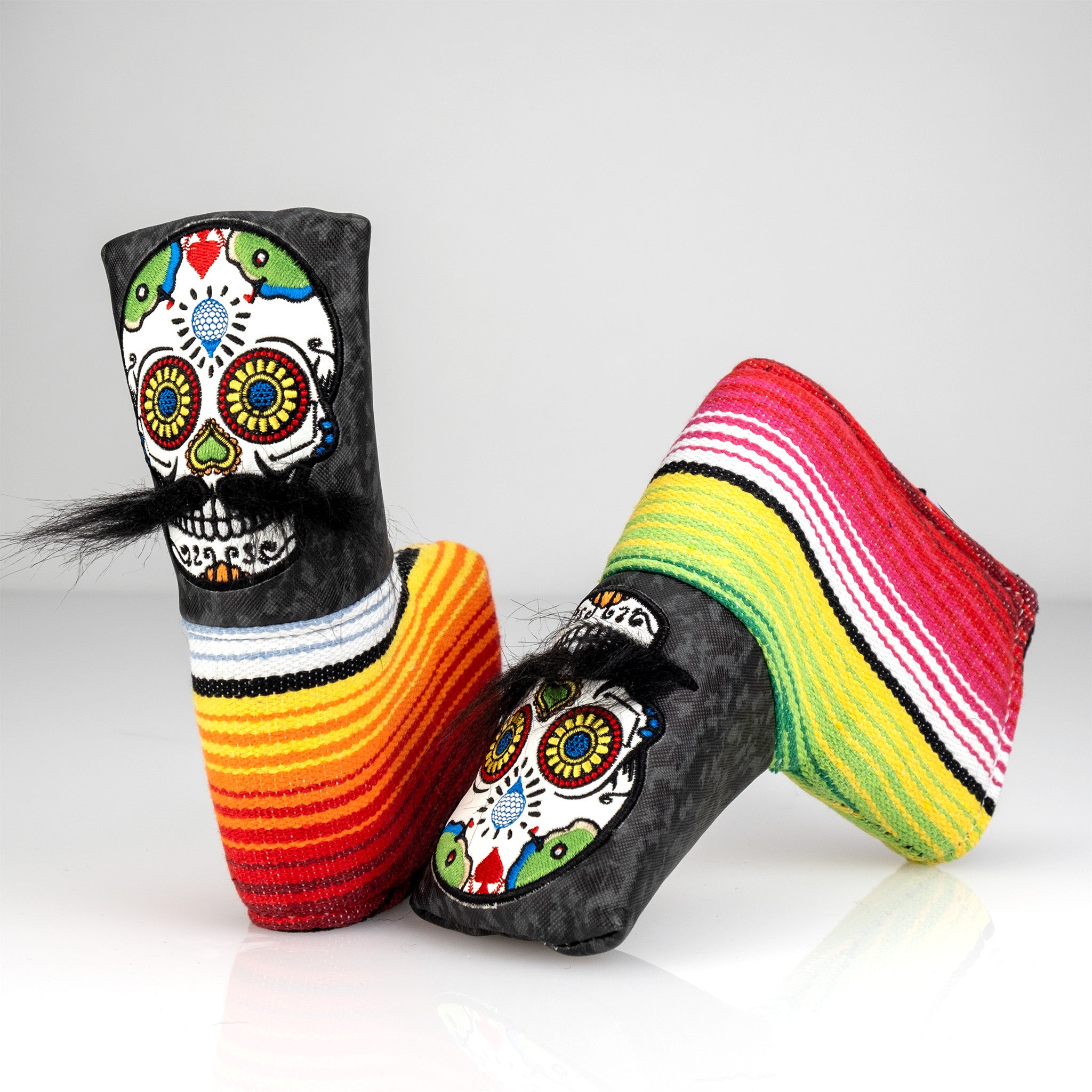 Colorful golf club headcovers with Día de los Muertos skull designs, paired with vibrant striped socks for bold golf style.