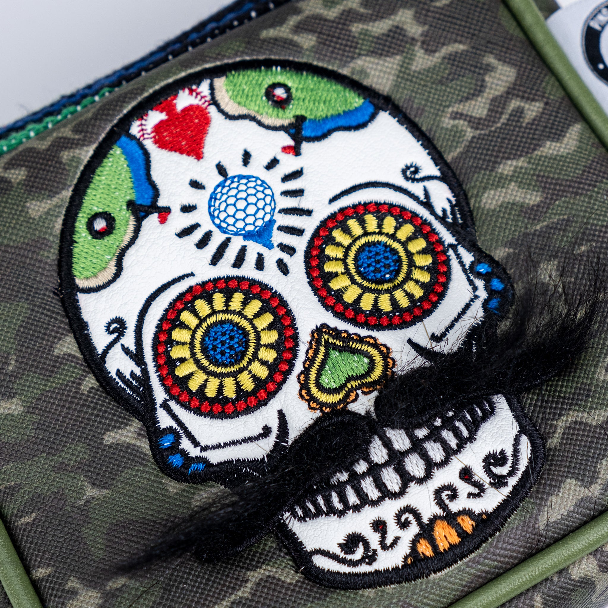 Colorful embroidered skull patch with floral accents, on camouflage fabric for bold, unique golf style.